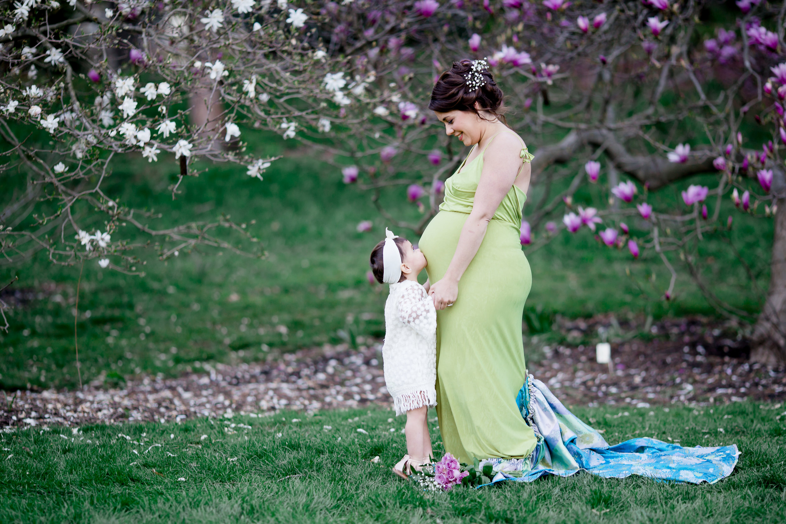 pregnant mom with older child kissing belly and mom looking at child with flowers in background