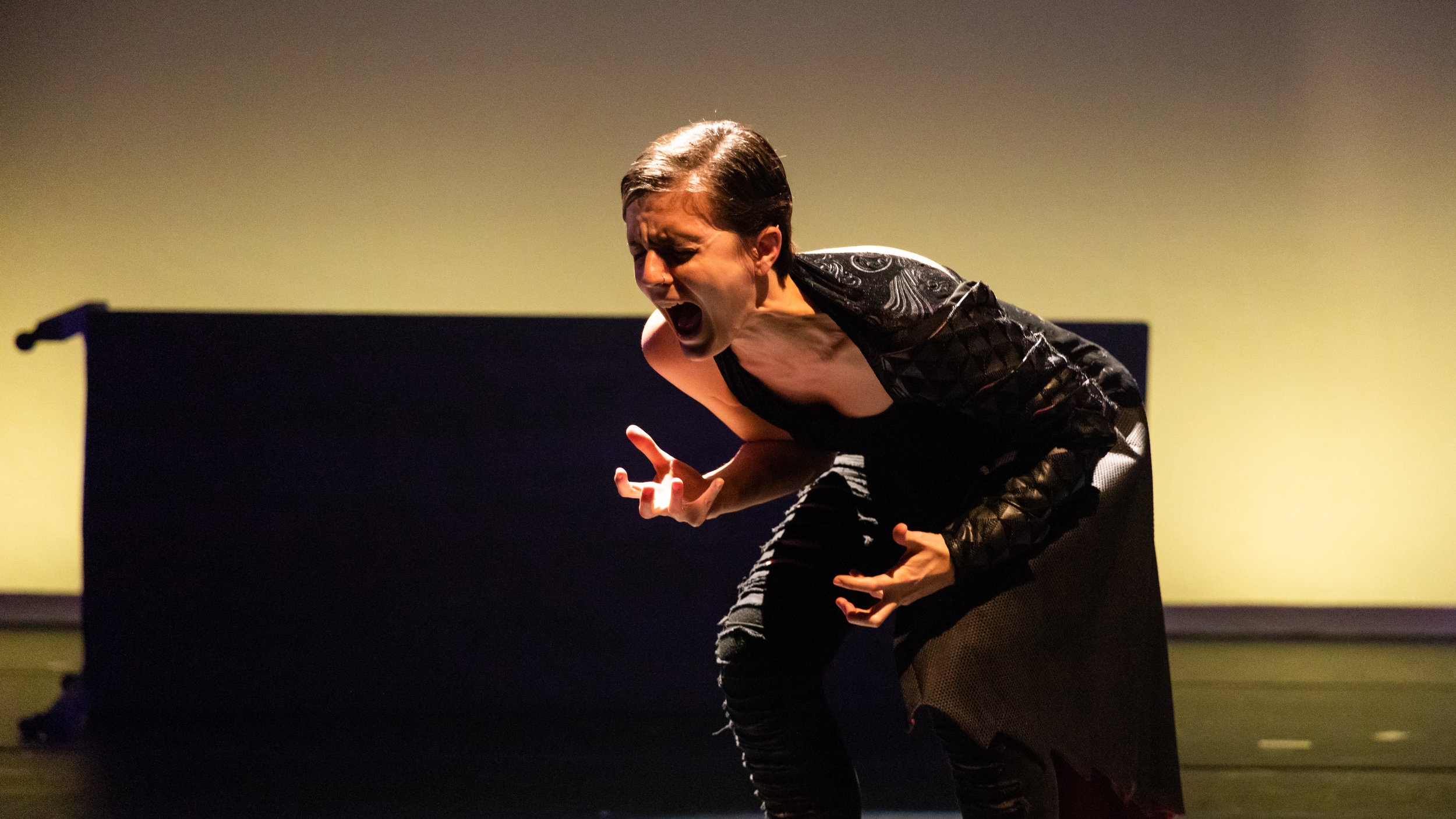 Photo by Jonathan Hsu: Christine screams silently, mouth open, hands gnarled. Her hair is short. The veins and muscles in her neck are taut and protruding. She wears an asymmetrical textured black costume. She is in her early 30’s in this photo.