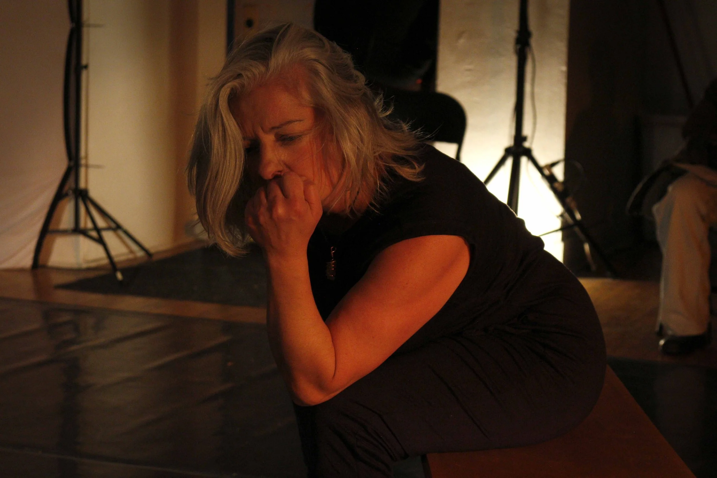 Tiffany leans her head against her hand, which is balled into a fist. She is hunched over and her eyes are downcast, brow furrowed, as if she is in pain