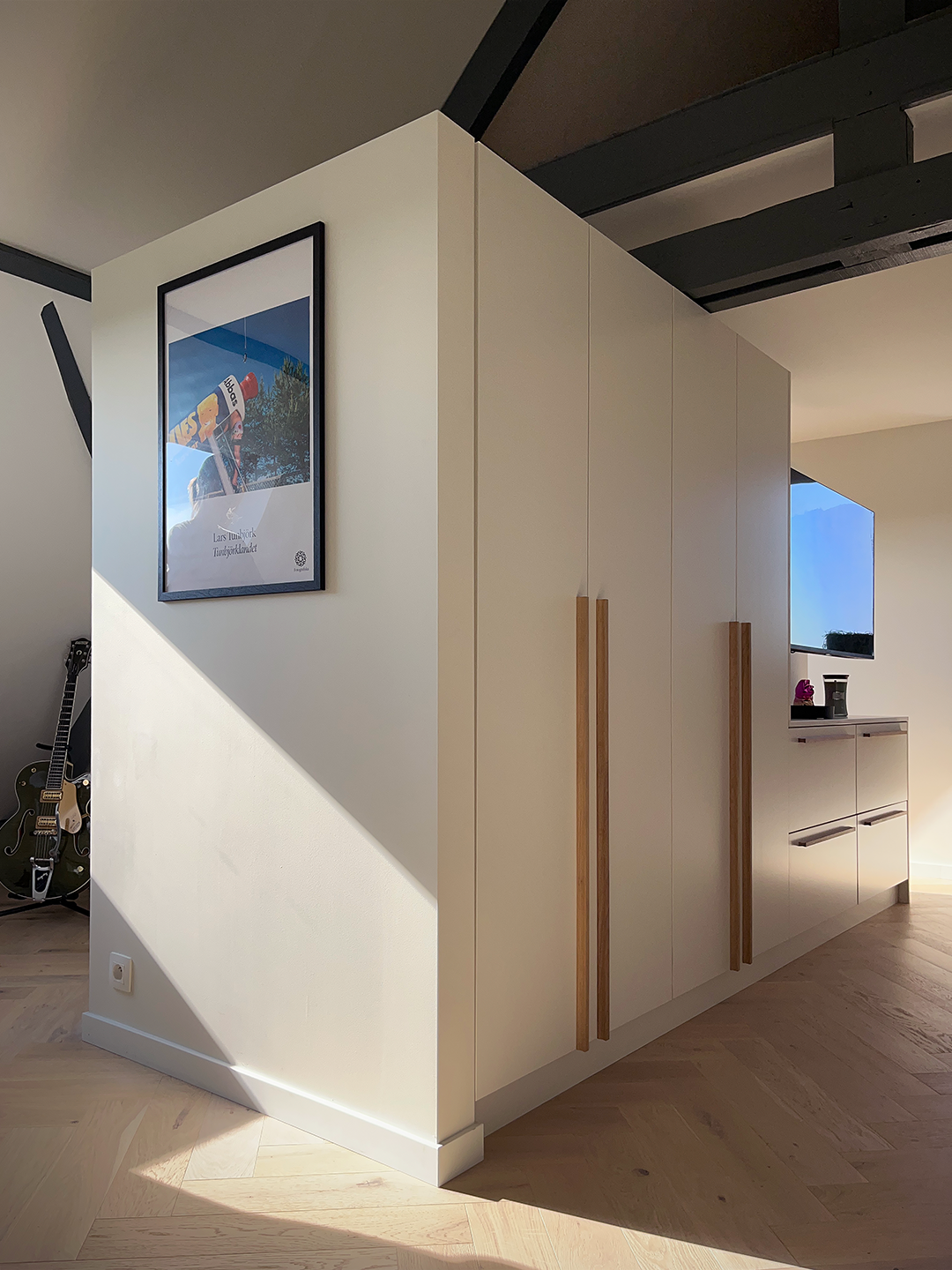 Grand module de dressing blanc et bois intégrant l'écran de télévision face au lit sous les toits
