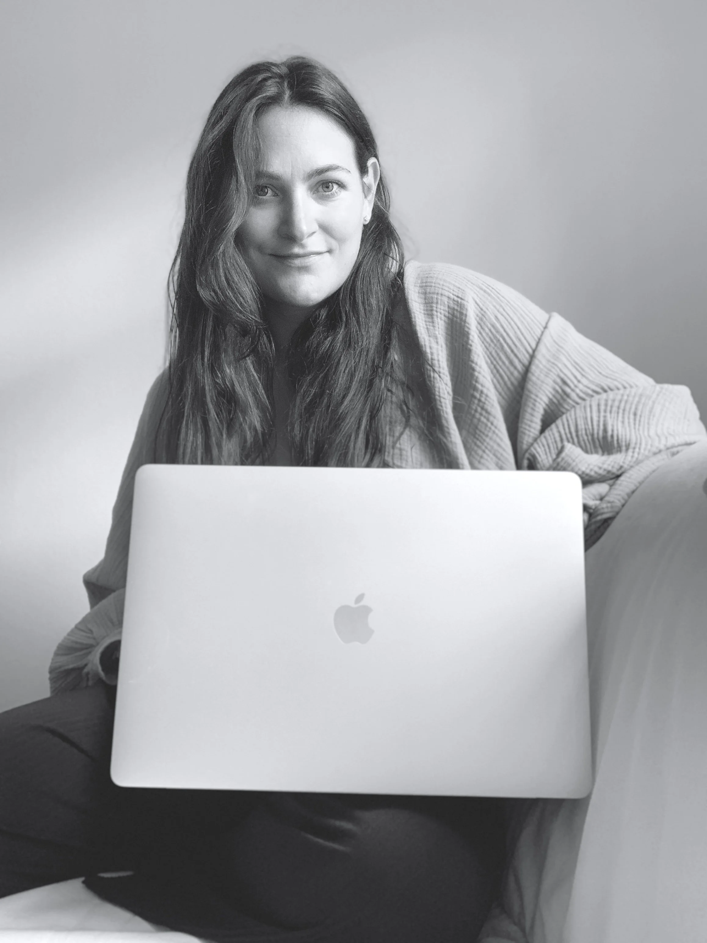 Writer, Alexis Mera Damen sitting on a sofa with her laptop.
