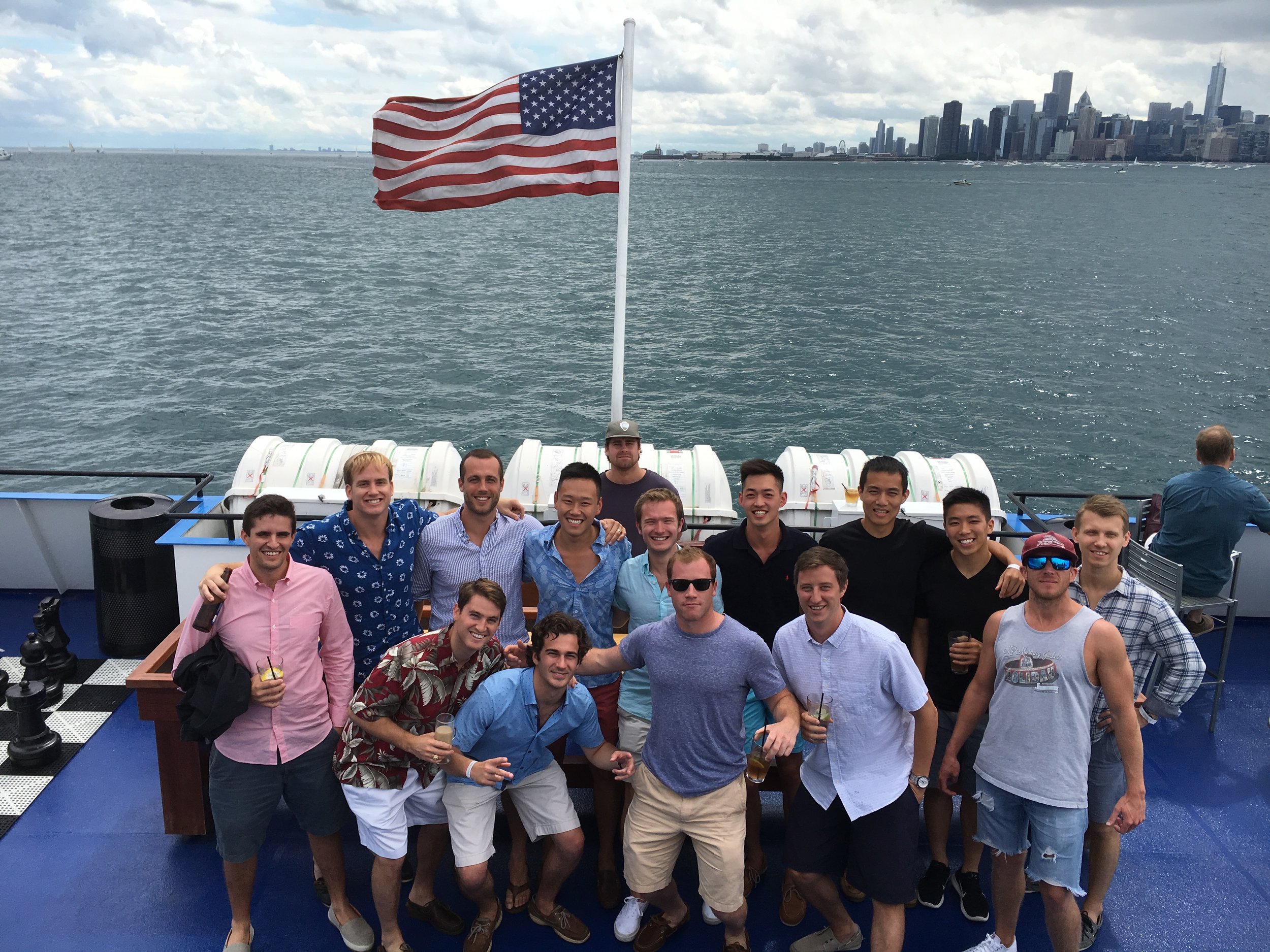 A group of people on a boat pose for a photo. An American flag and the Chicago skyline can be seen behind them.