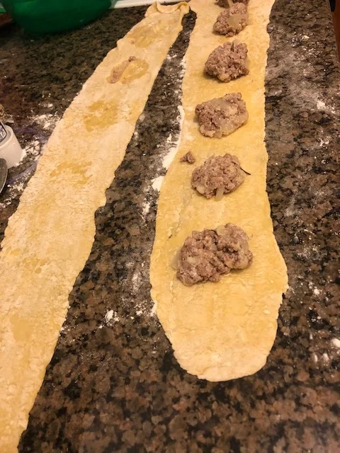 Take the additional sheet of ravioli/pasta dough and place it on top of the strip with the meat.Press down the dough around the meat mixture, making secure pockets.