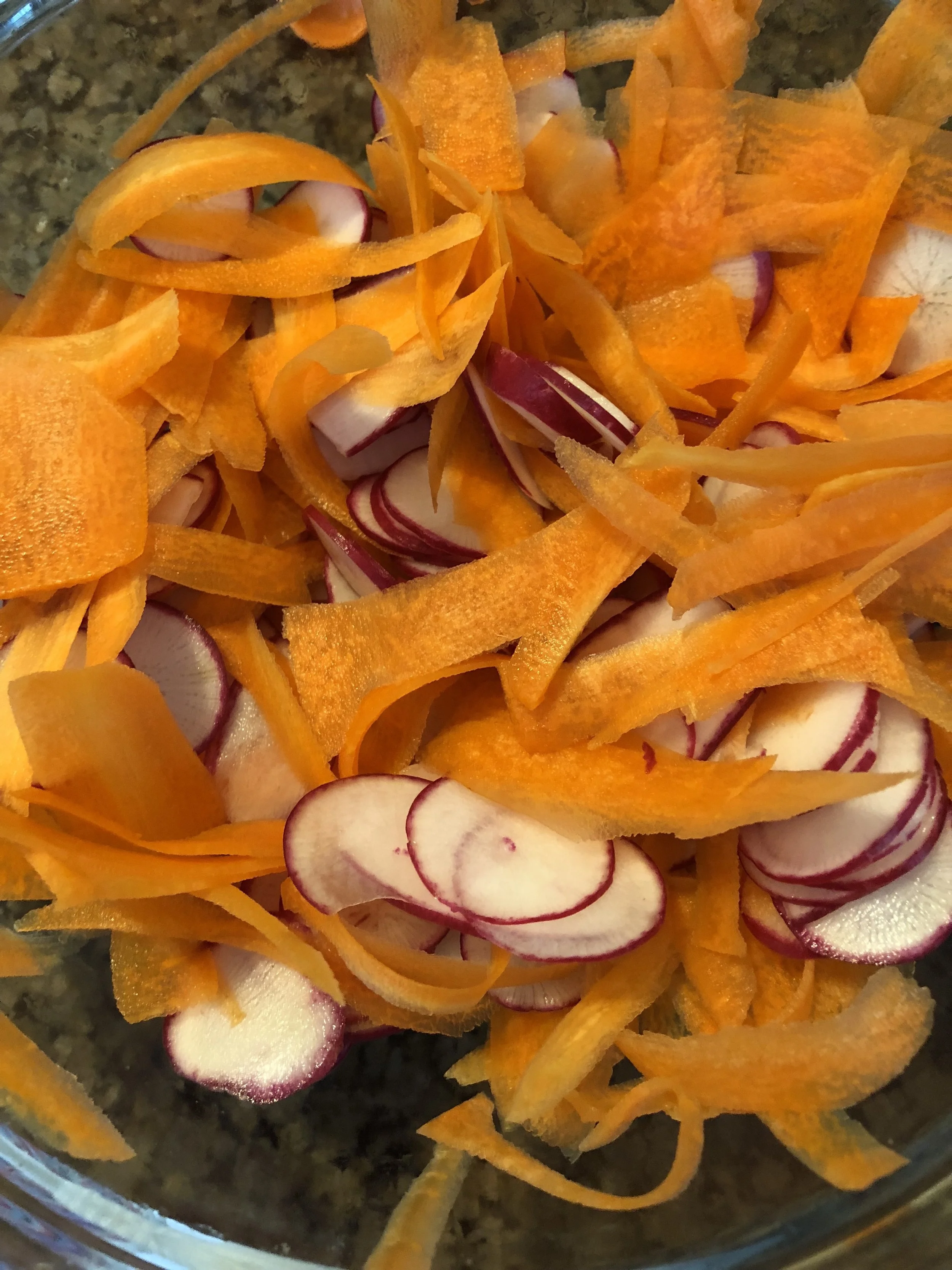 Using your vegetable peeler, peel the carrots into thin ribbons. In another bowl, mix the dressing by combining the honey, salt, pepper, lemon juice and oil. After mixing the dressing, toast the pepitas in a medium skillet by adding il, adding the seeds and covering in cumin. Add the dressing and diced scallions. Then roughly chop your cilantro after removing the leaves from the stems and add to the salad. Mix the salad throughly and then serve covered in a sprinkling of the toasted cumin pepitas.