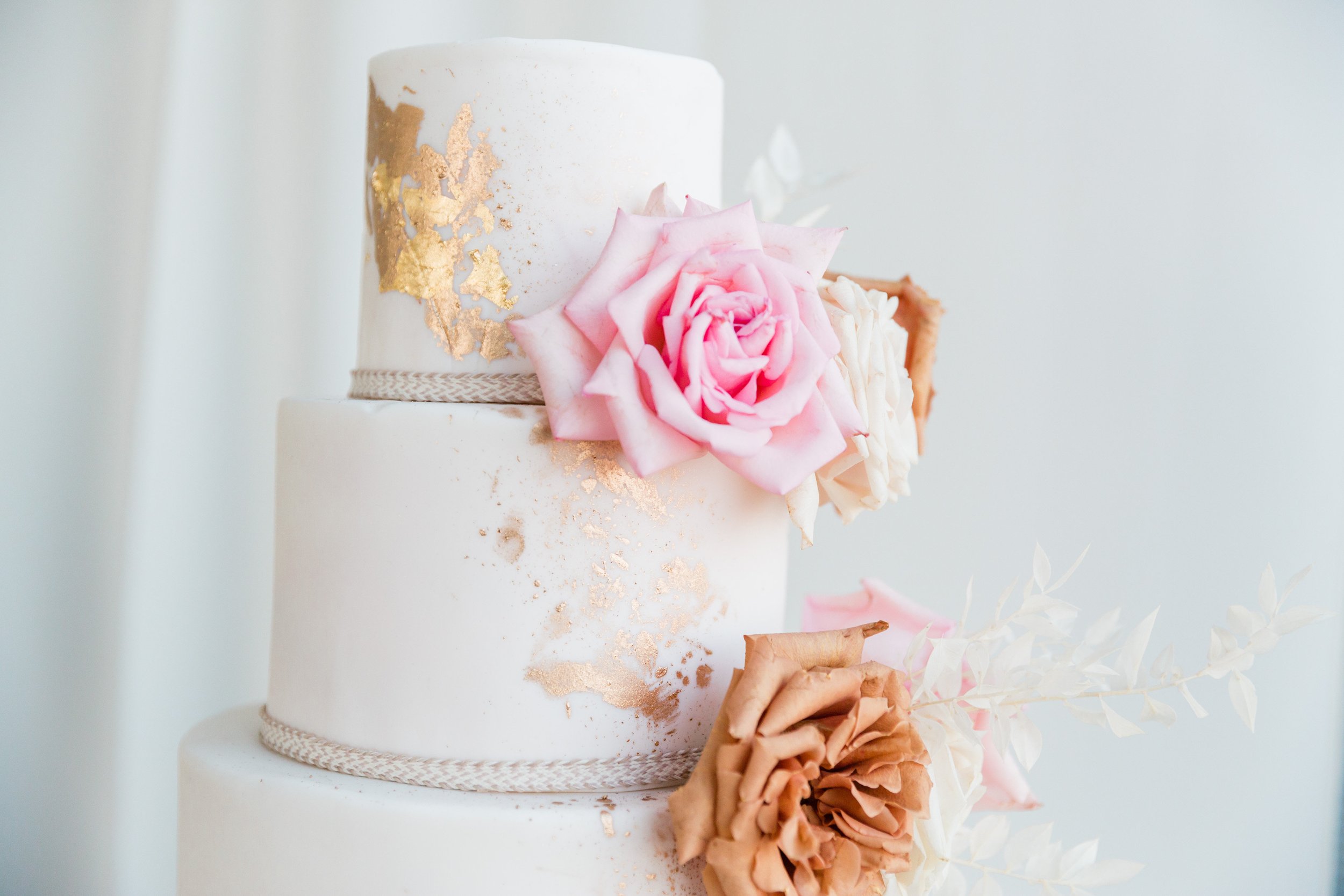 Three tier white wedding cake with gold foil and pink, white, and toffee roses