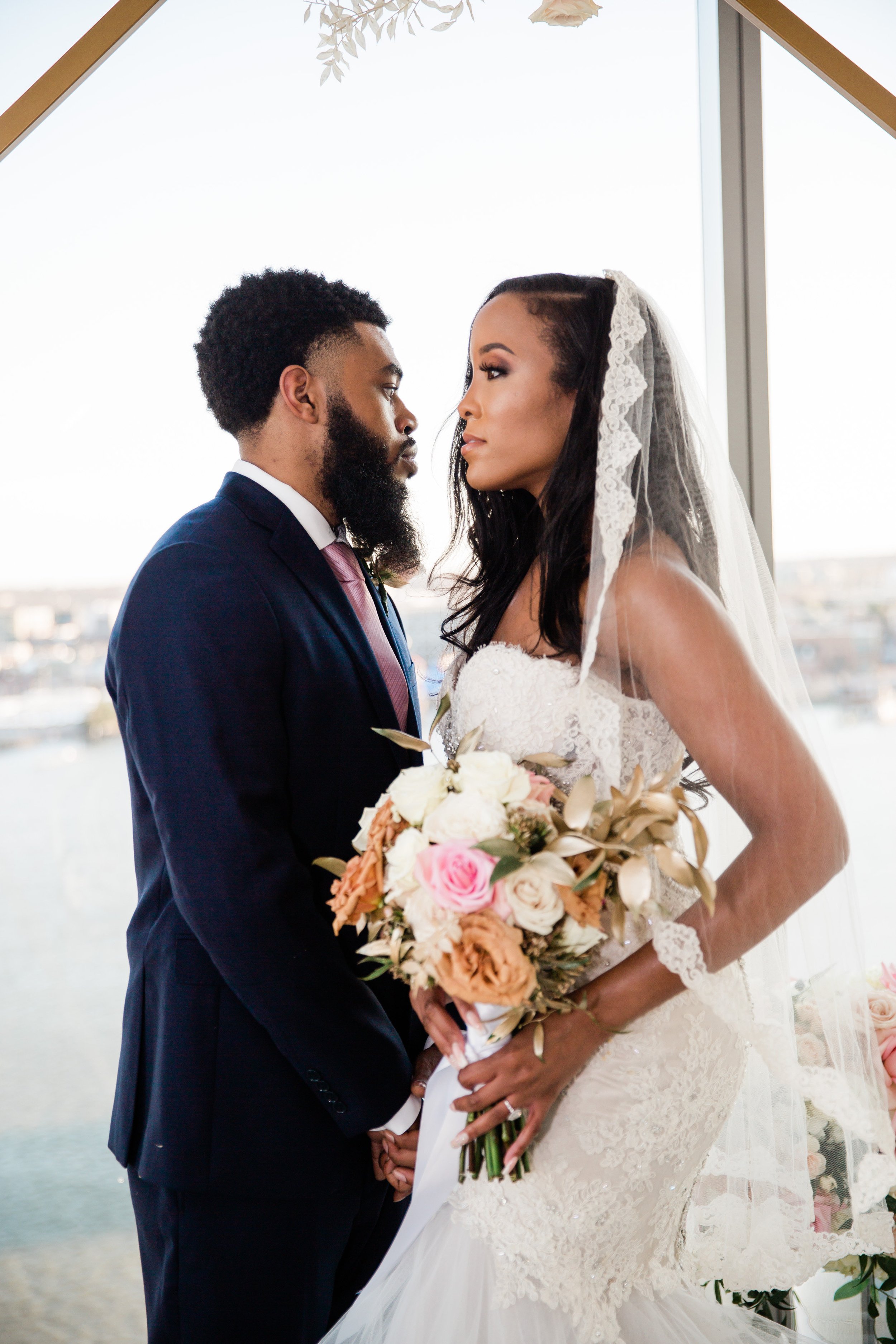 Black groom and bride facing each other in front of a window 