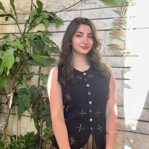 Portrait of Razan, Social Media Management, standing in front of green plants and a stone wall.