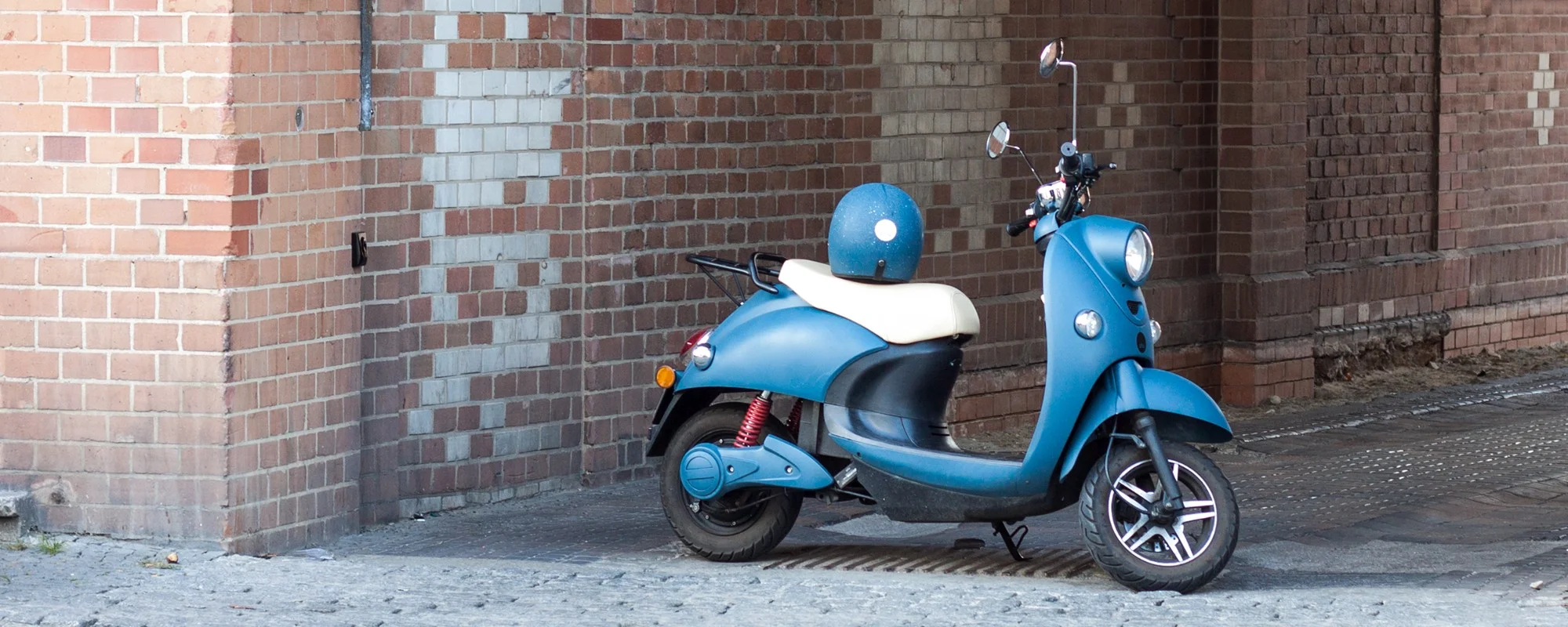 Lichtblauwe unu scooter met op de achtergrond een muurtje