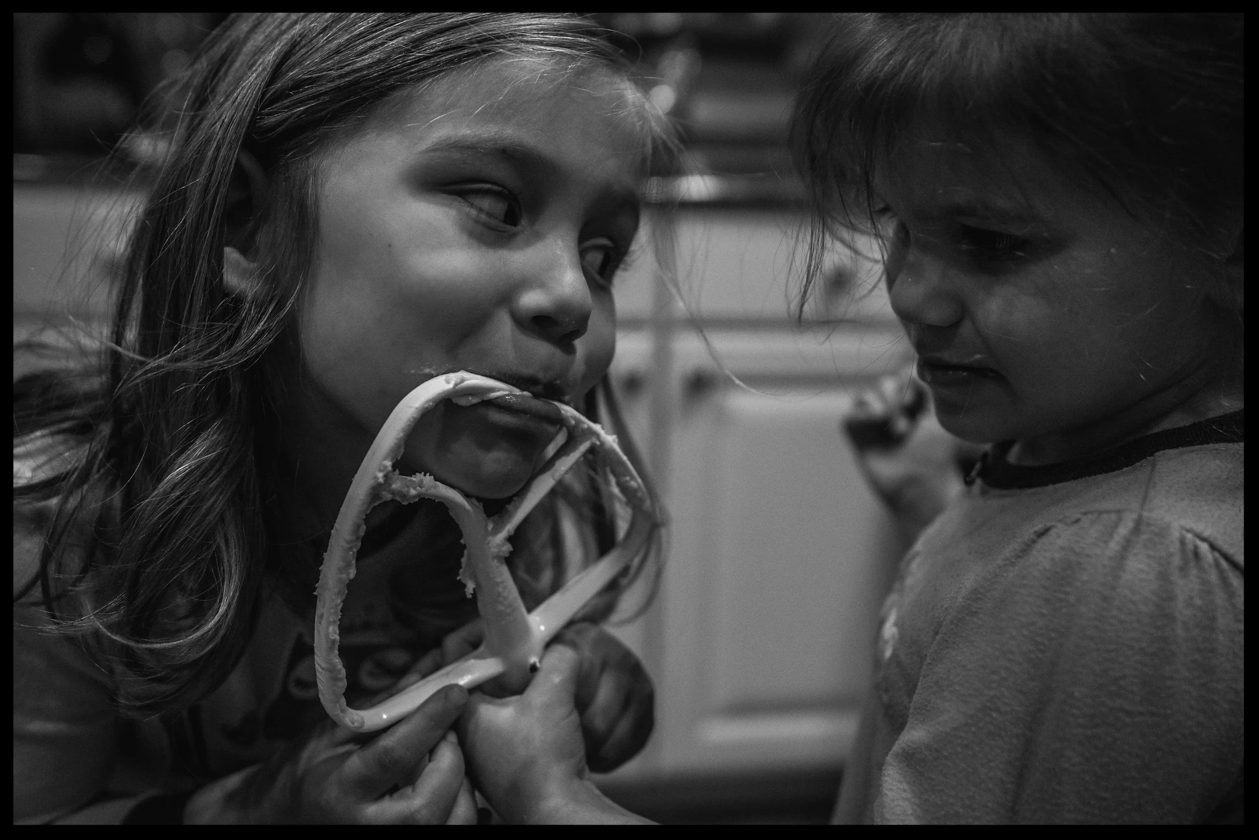 Sisters taking turns licking the beater, black and white