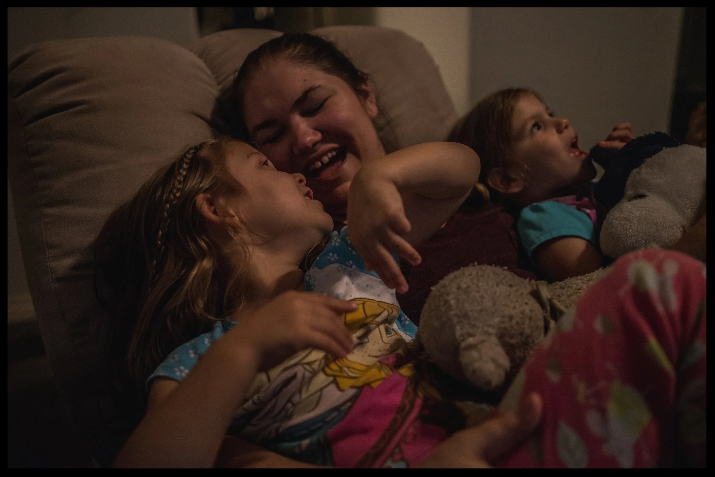 Mommy singing with her two daughters in the recliner before bedtime, color