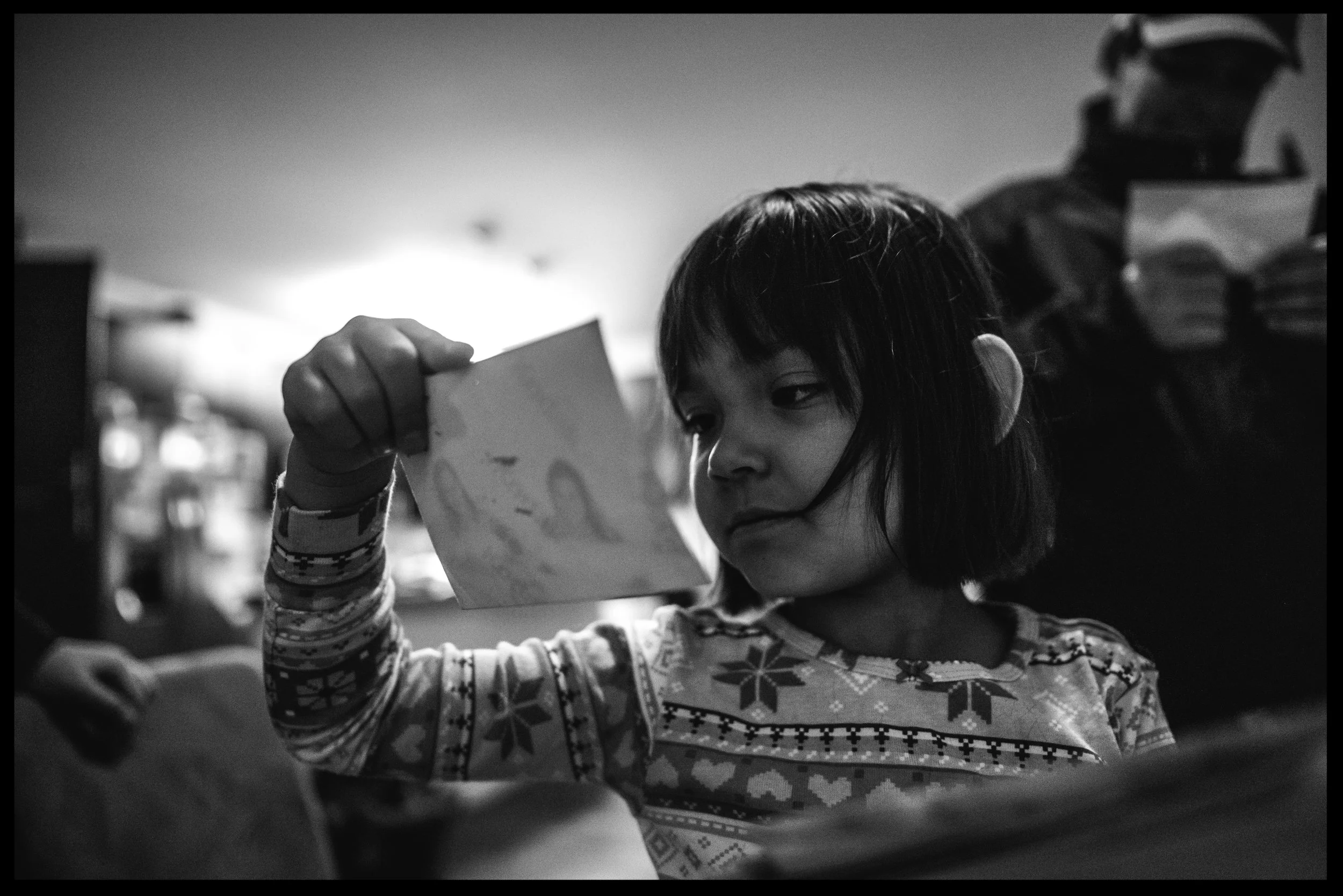 Little girl chewing on her hair and looking at family photos, black and white, Lakewood, Colorado