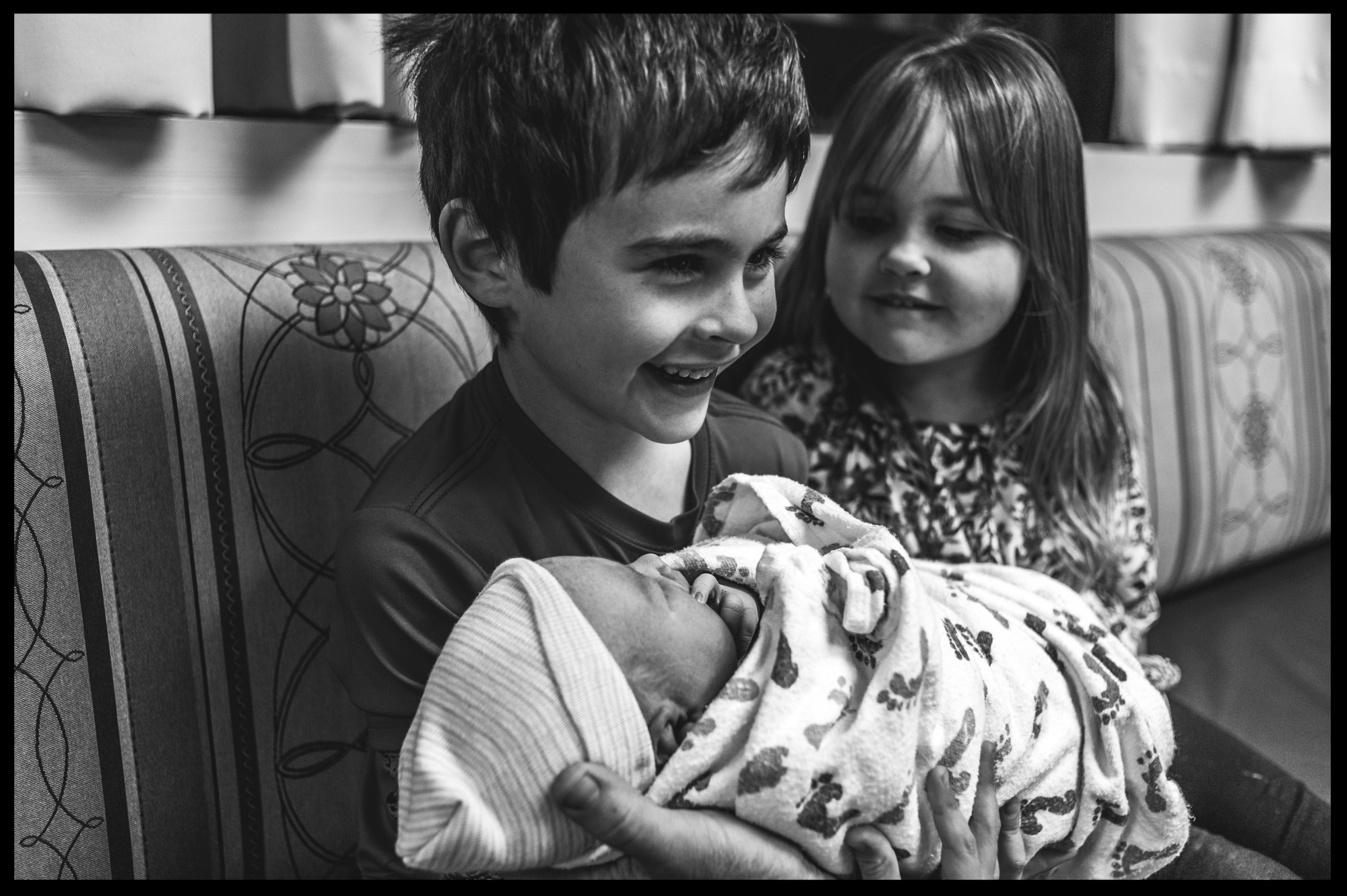 Little boy holding his new baby sister while his other sister looks on, black and white, Stillwater, OK