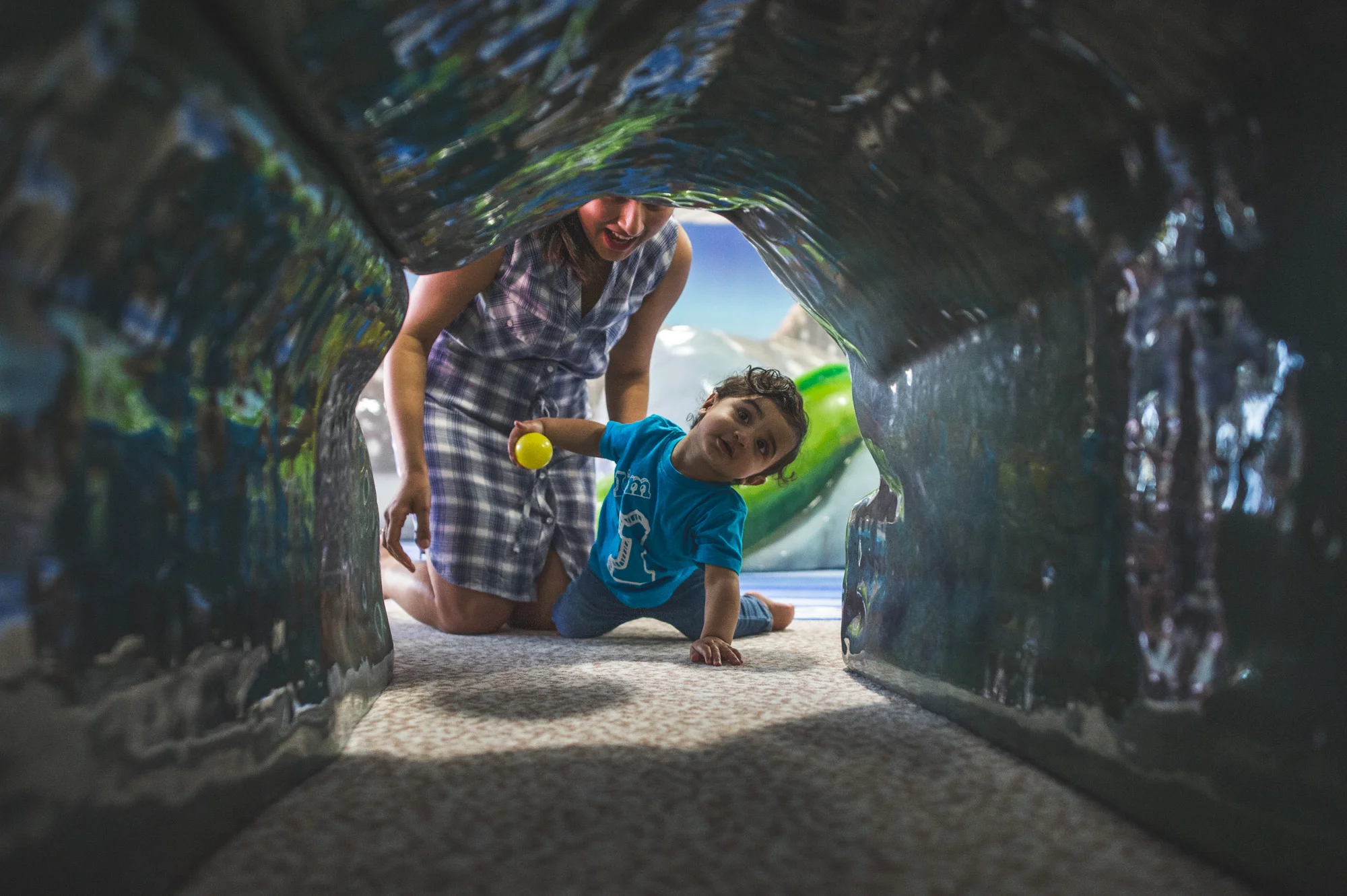 One year old crawls through a tunnel at the birthday party room at the Denver Aquarium while his mother encourages him