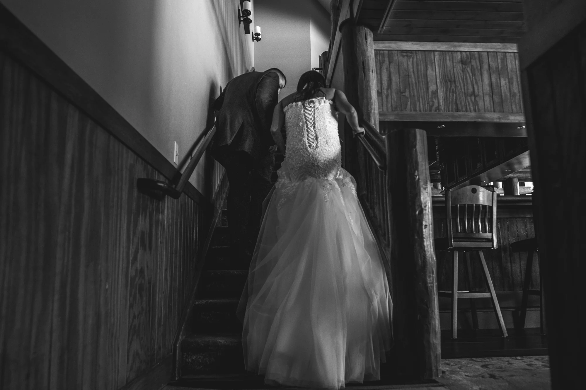 Bride and groom walk up the stairs as the bride's dress flows down the steps, Estes Park, CO, black and white