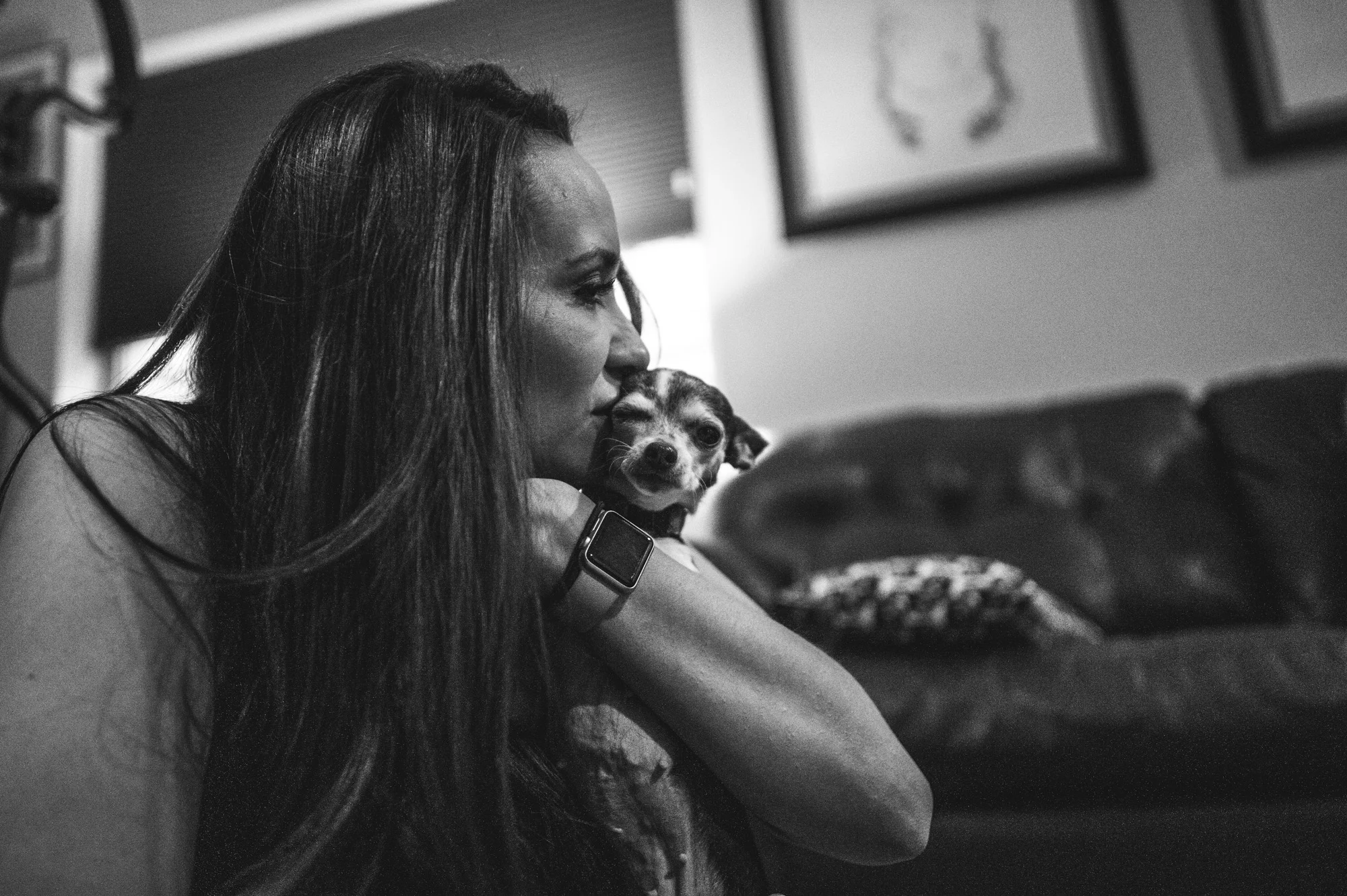 Woman kissing her chihuahua's face as the little dog makes a funny face, black and white, Denver, Colorado