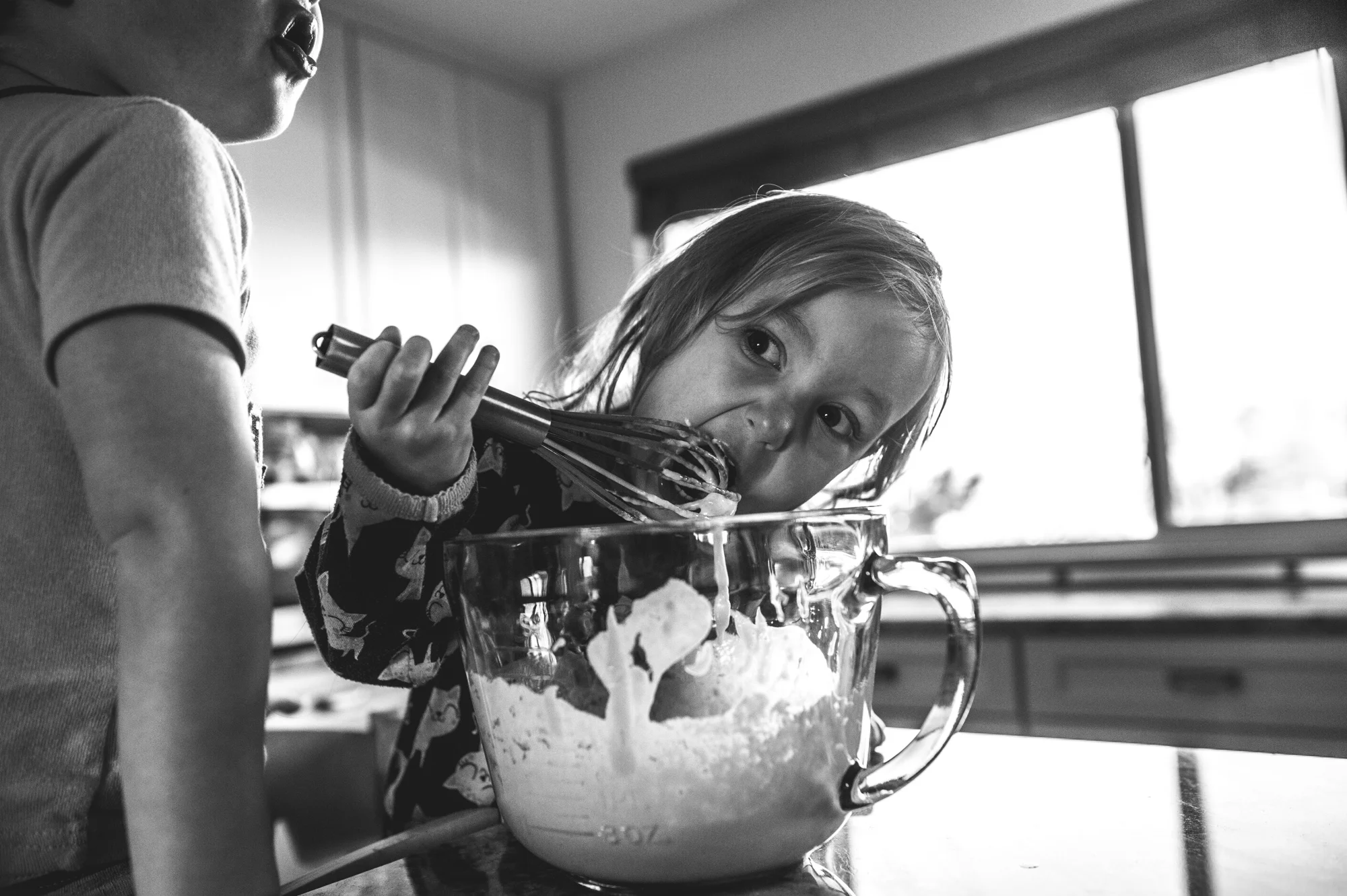 Little girl eating pancake batter off of a whisk out of the bowl, black and white, Denver, Colorado