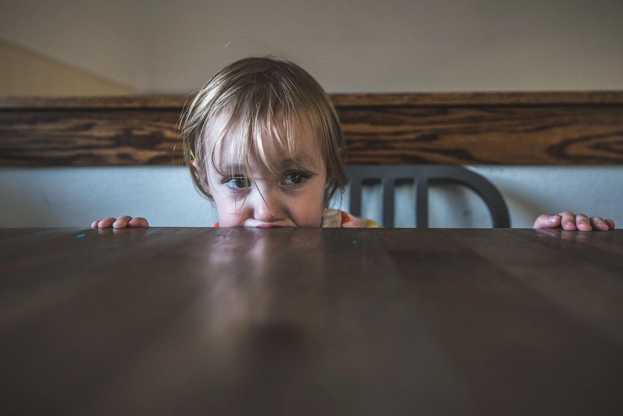 Close up of a little girl putting her mouth on the edge of the table during a half day in the life session in Denver, Colorado