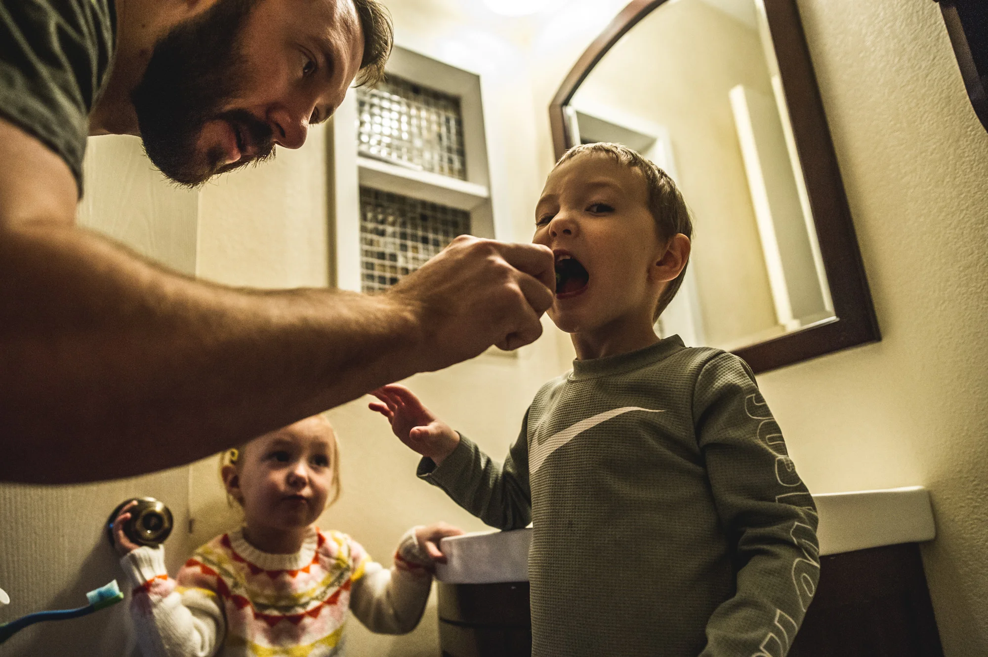 Father leans over to brush his young son's teeth as their young daughter looks on, color, Denver, Colorado