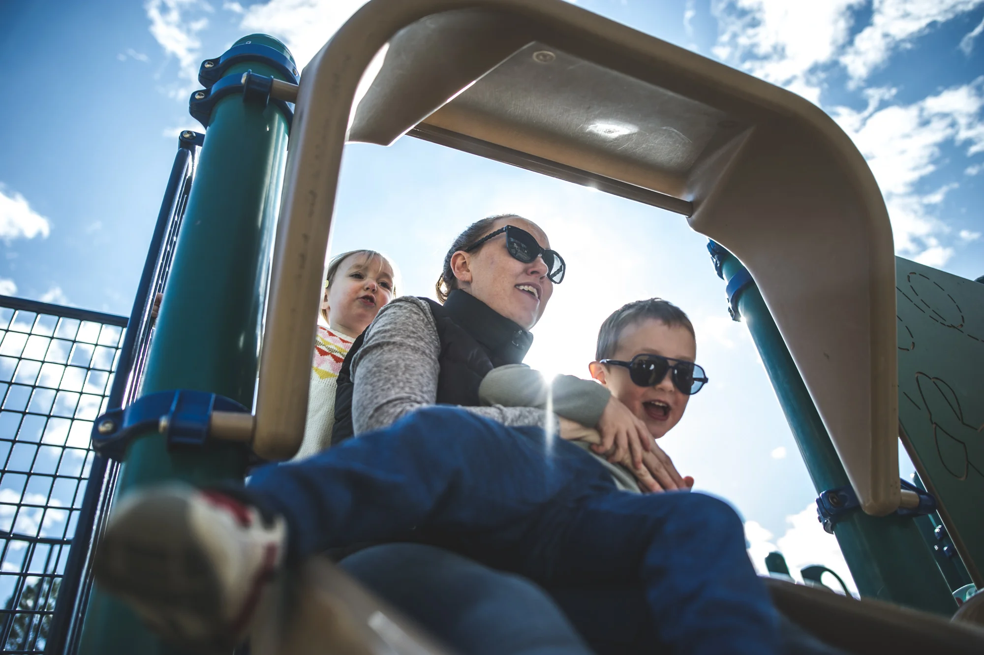 Close up of a young boy sitting on his mother's lap at the top of a slide while his sister stands behind her, color, Denver, Colorado