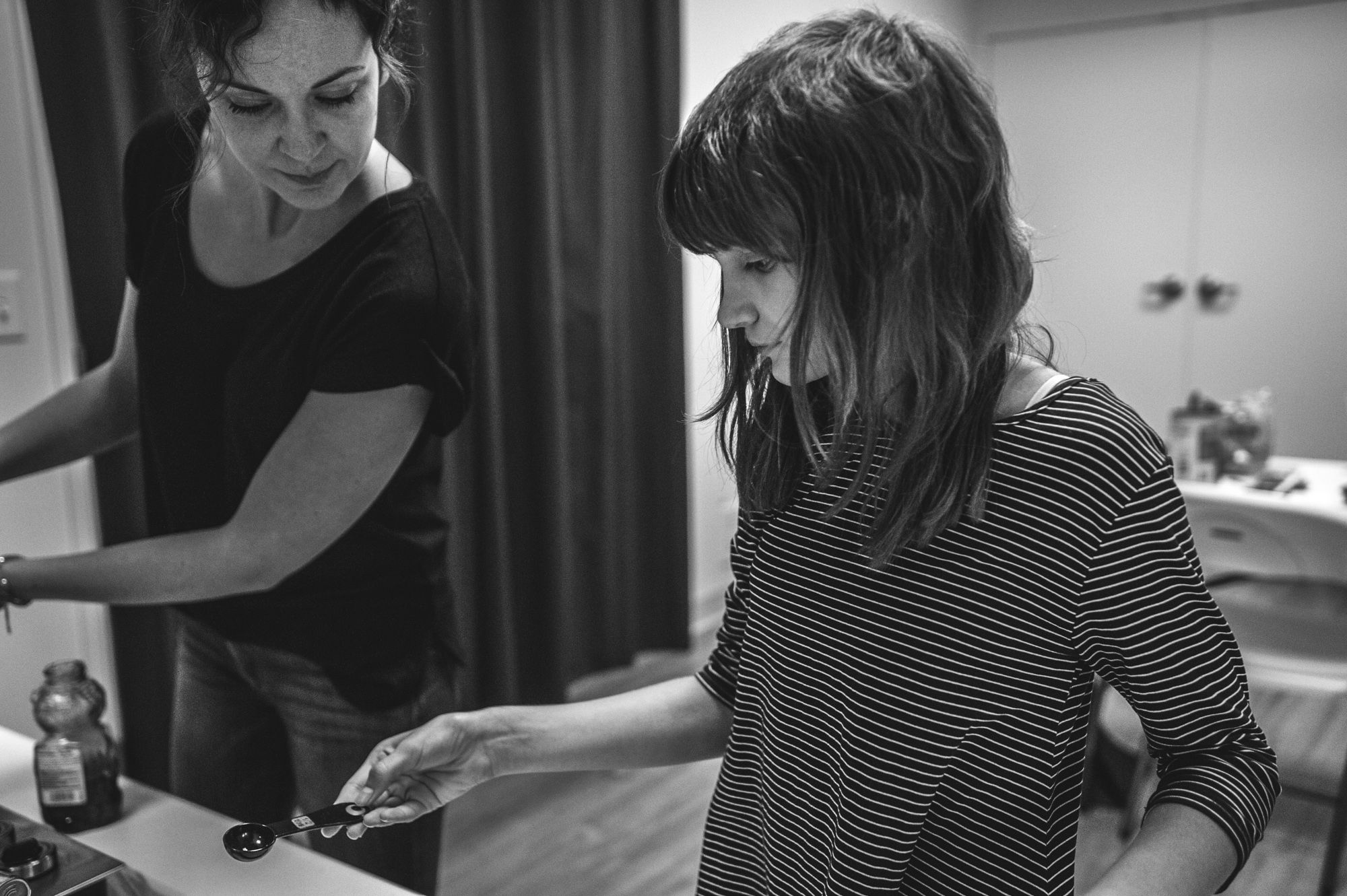 Cooking teacher leans over to help her student read a measuring spoon during a healthy cooking class with spectrum yoga in Denver, Colorado, black and white