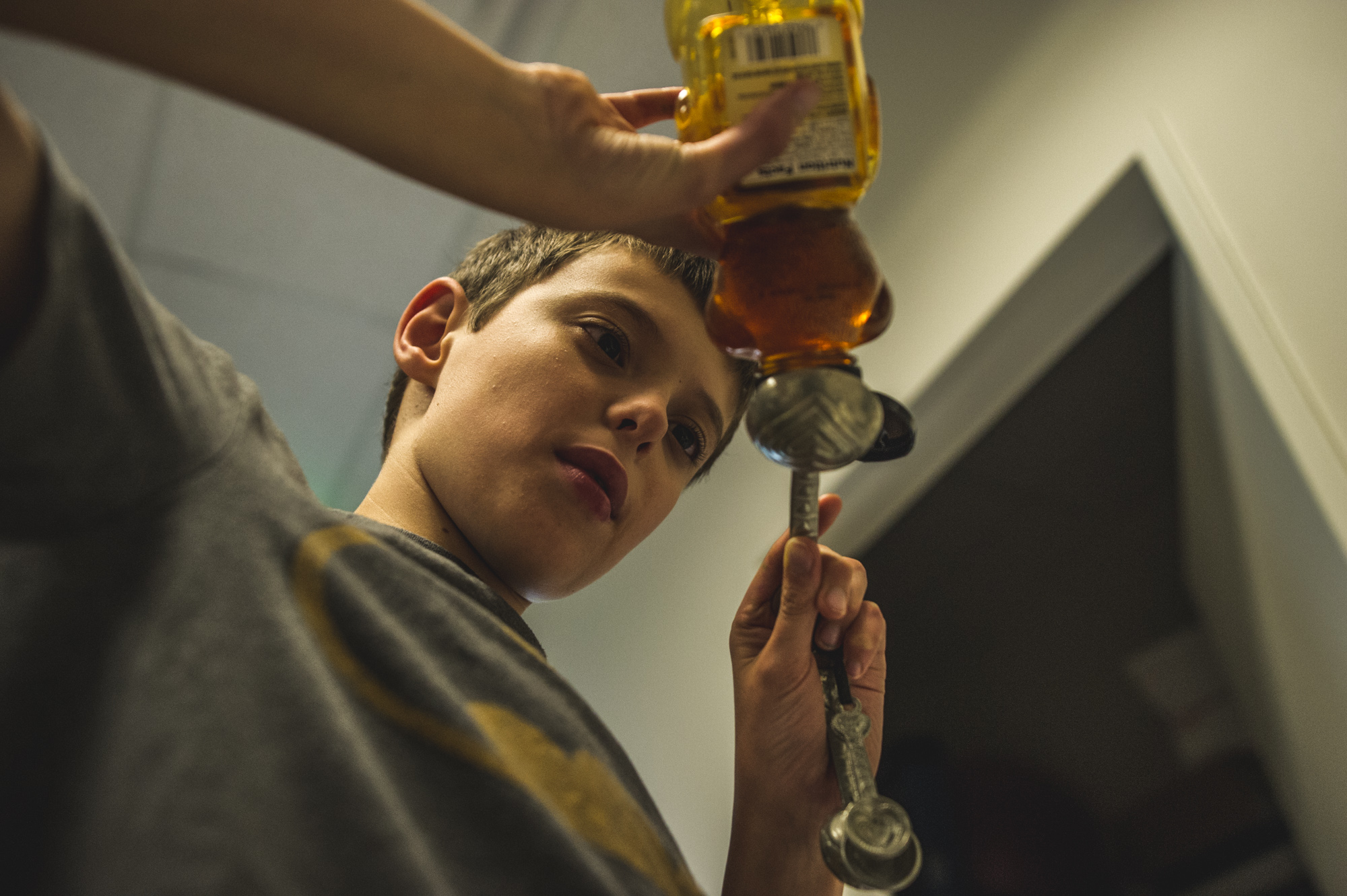 Underneath shot of a boy in a batman shirt pouring honey into a measuring spoon during a cooking class in Littleton, Colorado, color