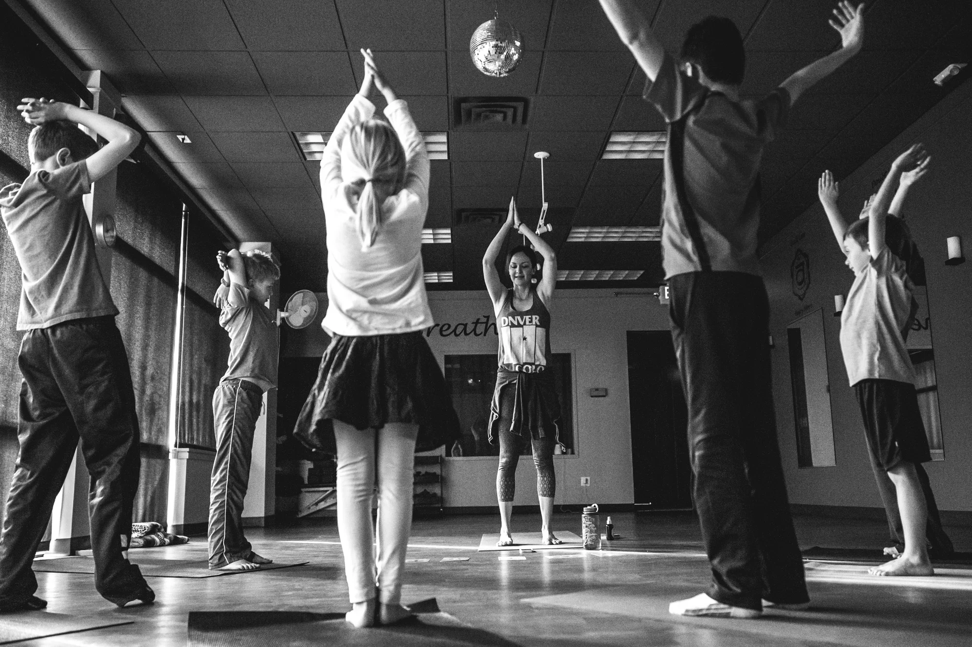 The whole class does a yoga pose with their hands over their heads during a yoga class for students with autism in Highland's Ranch, Colorado, black and white
