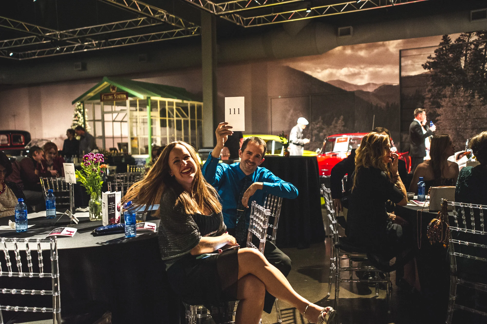 A woman turns her head and laughs as the man she is with hold up an auction paddle in the middle of a friendly bidding war at the Autism Society's Winter Fundraiser at the Vehicle Vault in Parker, Colorado. Photo is in color.