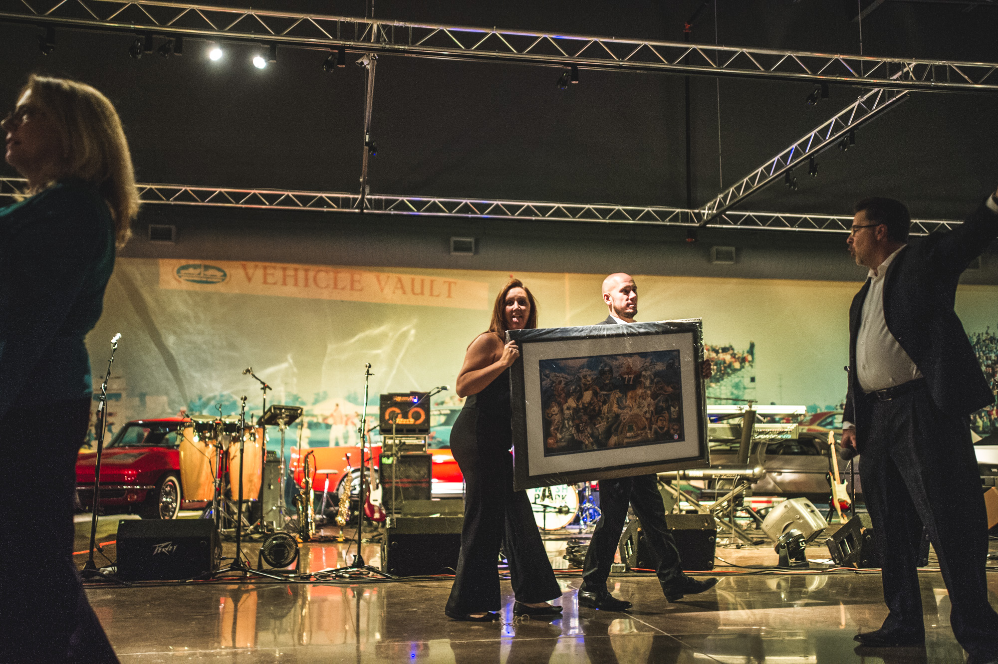 A woman and a man hold a giant framed auction item at the Vehicle Vault in Parker, Colorado. Color.