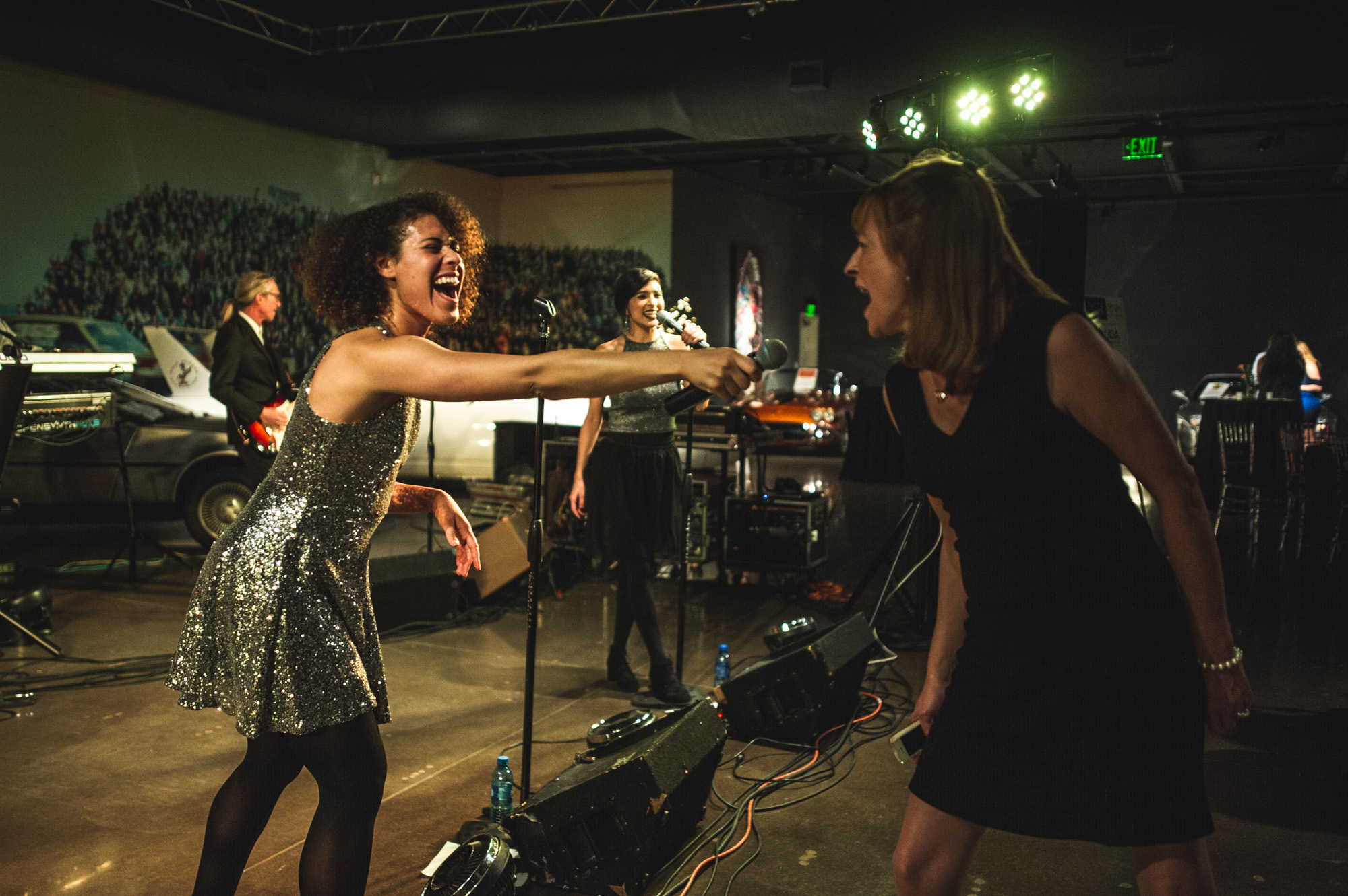 A woman sings into the microphone being held out by one of the vocalists of the Wash Park Band, Parker, CO, color