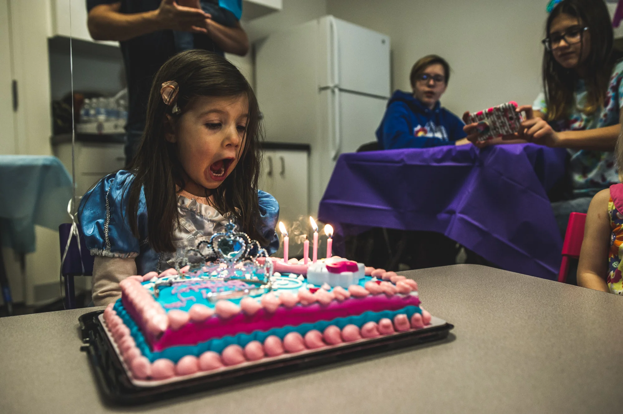 Little girl blows out four candles on her pink and blue birthday cake as she wears a princess dress at her birthday party at Family Connections kids' gym in Littleton, Colorado