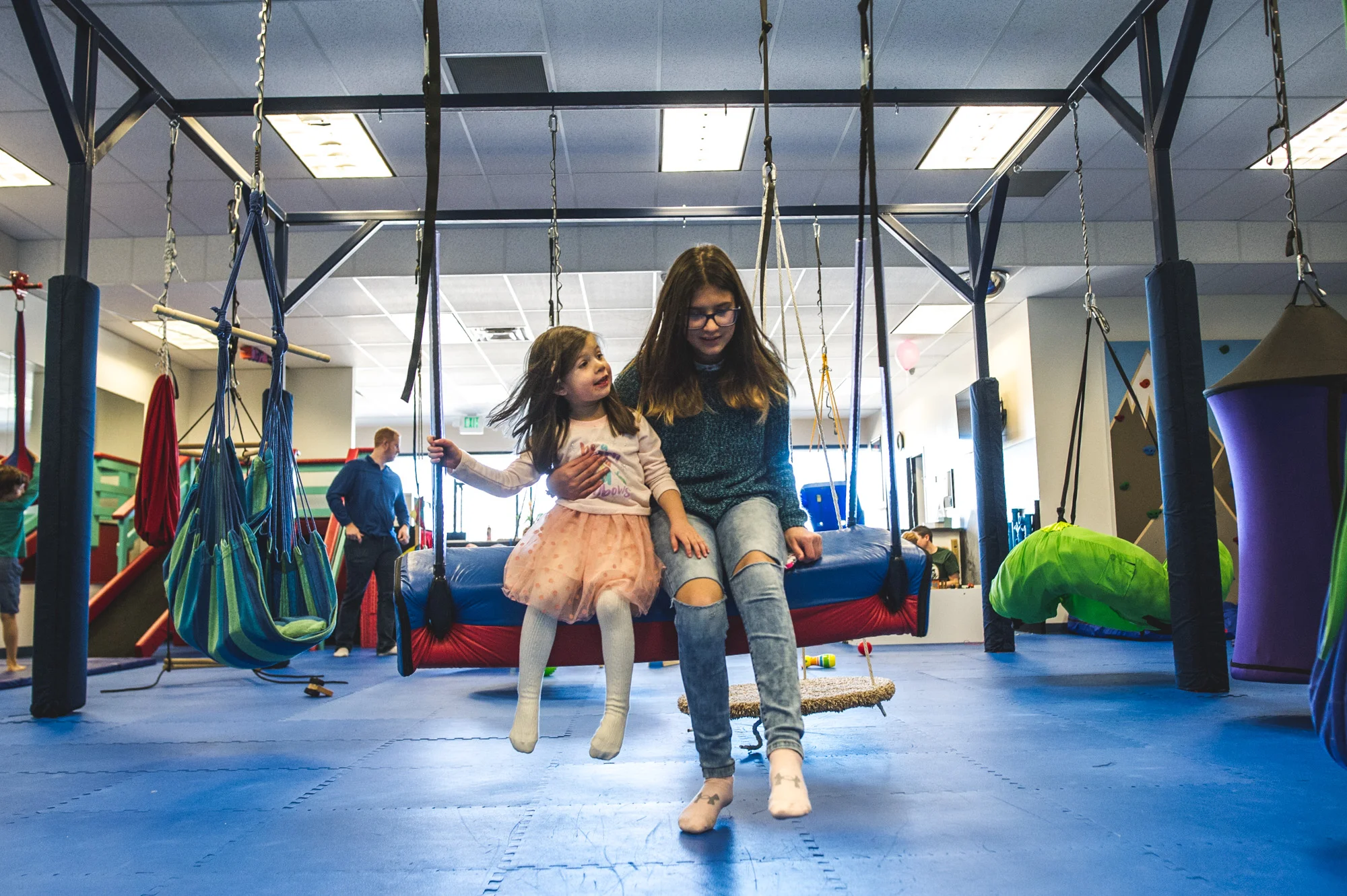 Little girl swings on a big swing with an older girl at a kid's gym in Littleton, Colorado. Photo is in color.