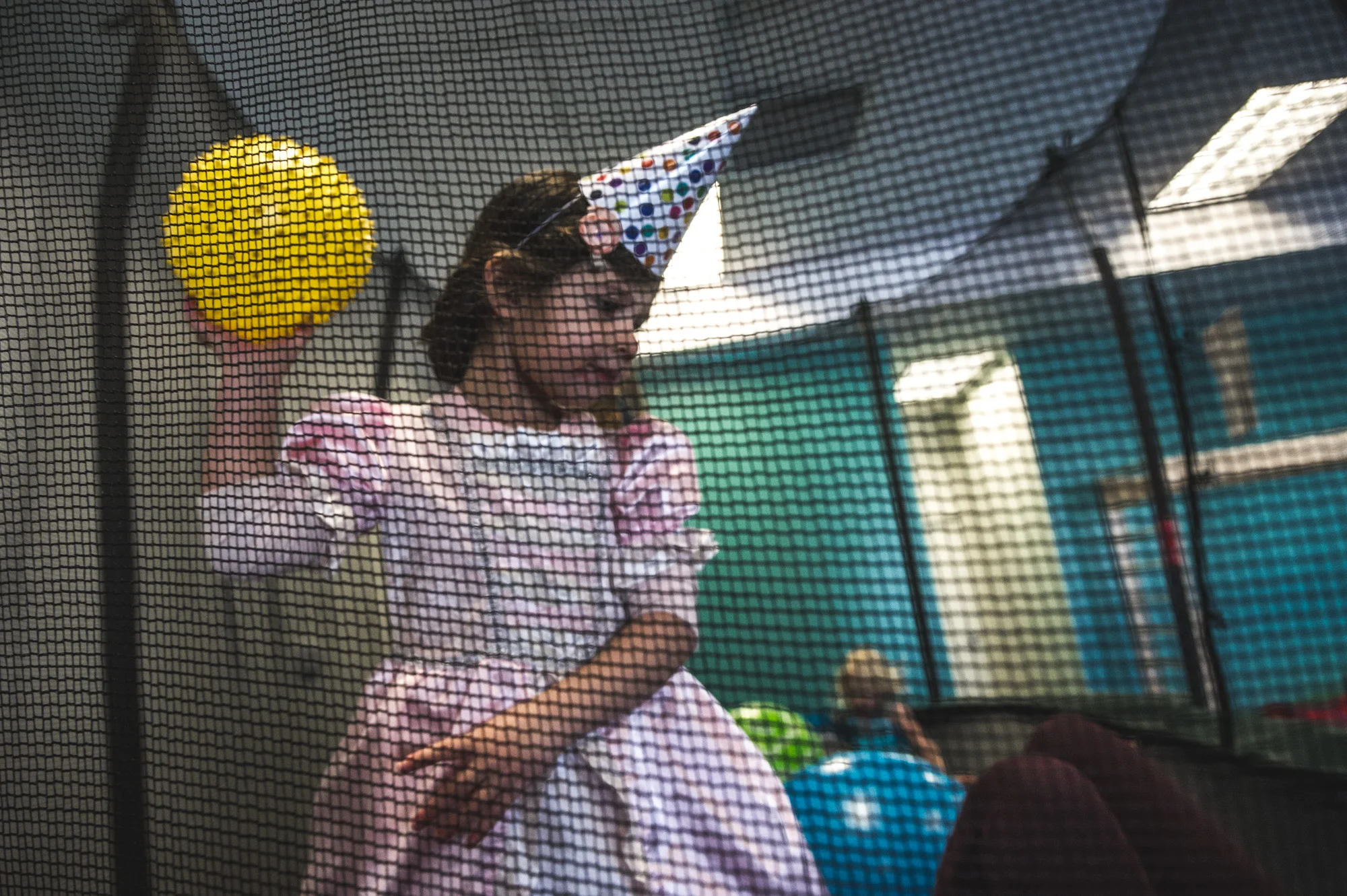 Little girl in a party hat and princess outfit aims a yellow ball at her friend on a trampoline at Family Connections Thera-play gym in Littleton, Colorado.