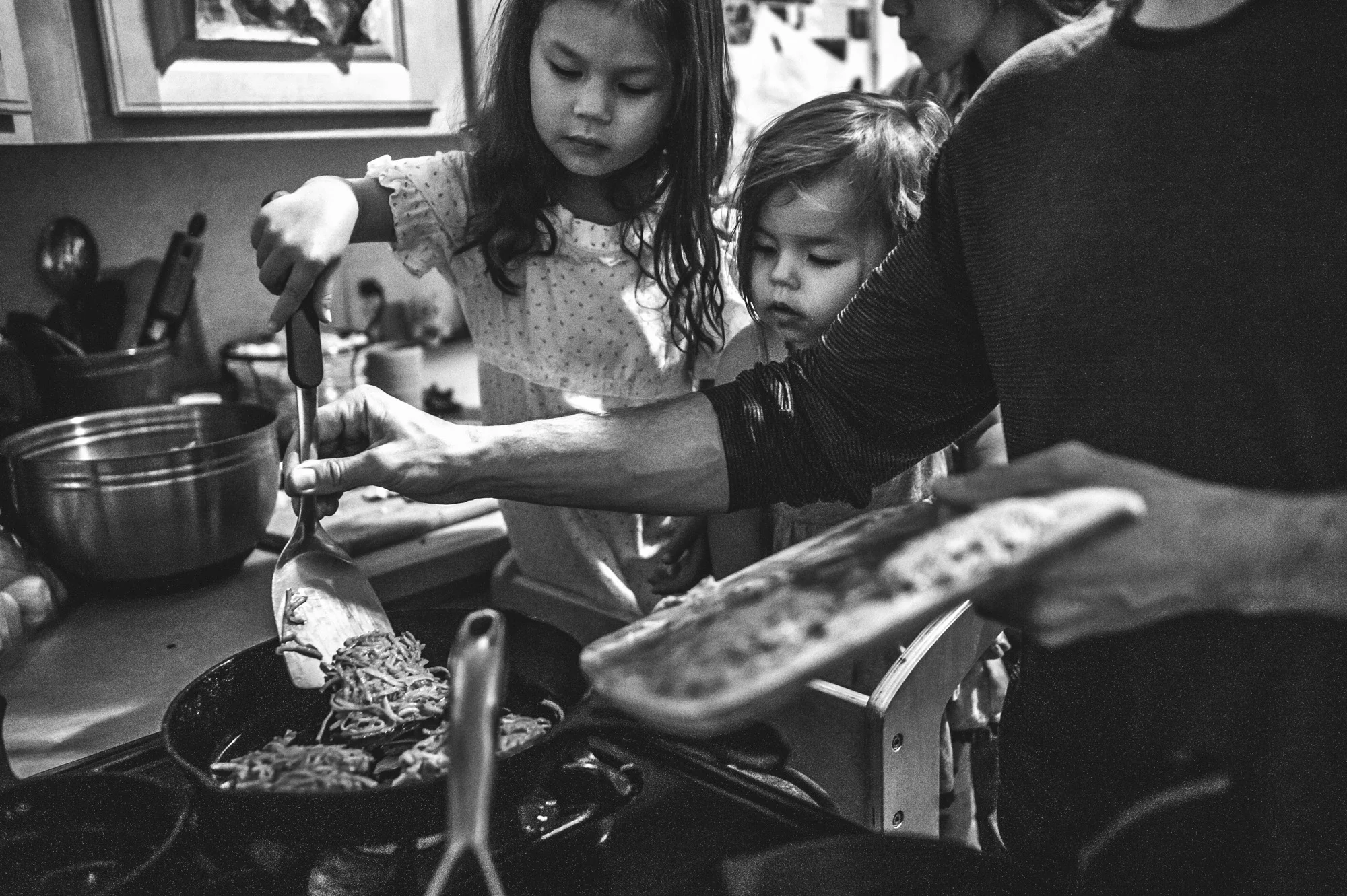 Black and white photo of a father and his two little girls cooking latkes together for Hanukkah in Denver, Colorado