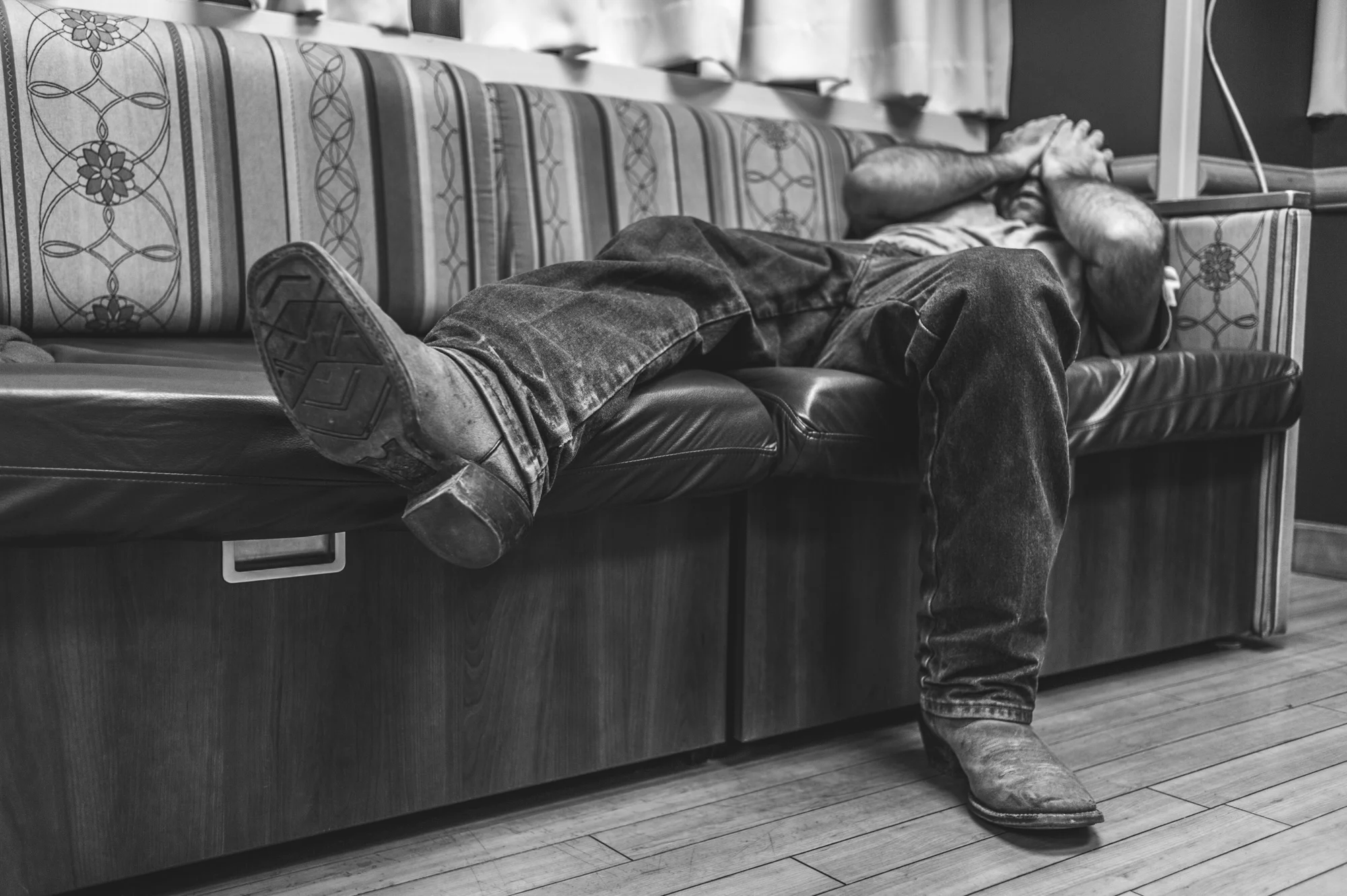 Black and white photo of an expectant father lying on the couch, waiting for the birth of his child, and rubbing his eyes in exhaustion
