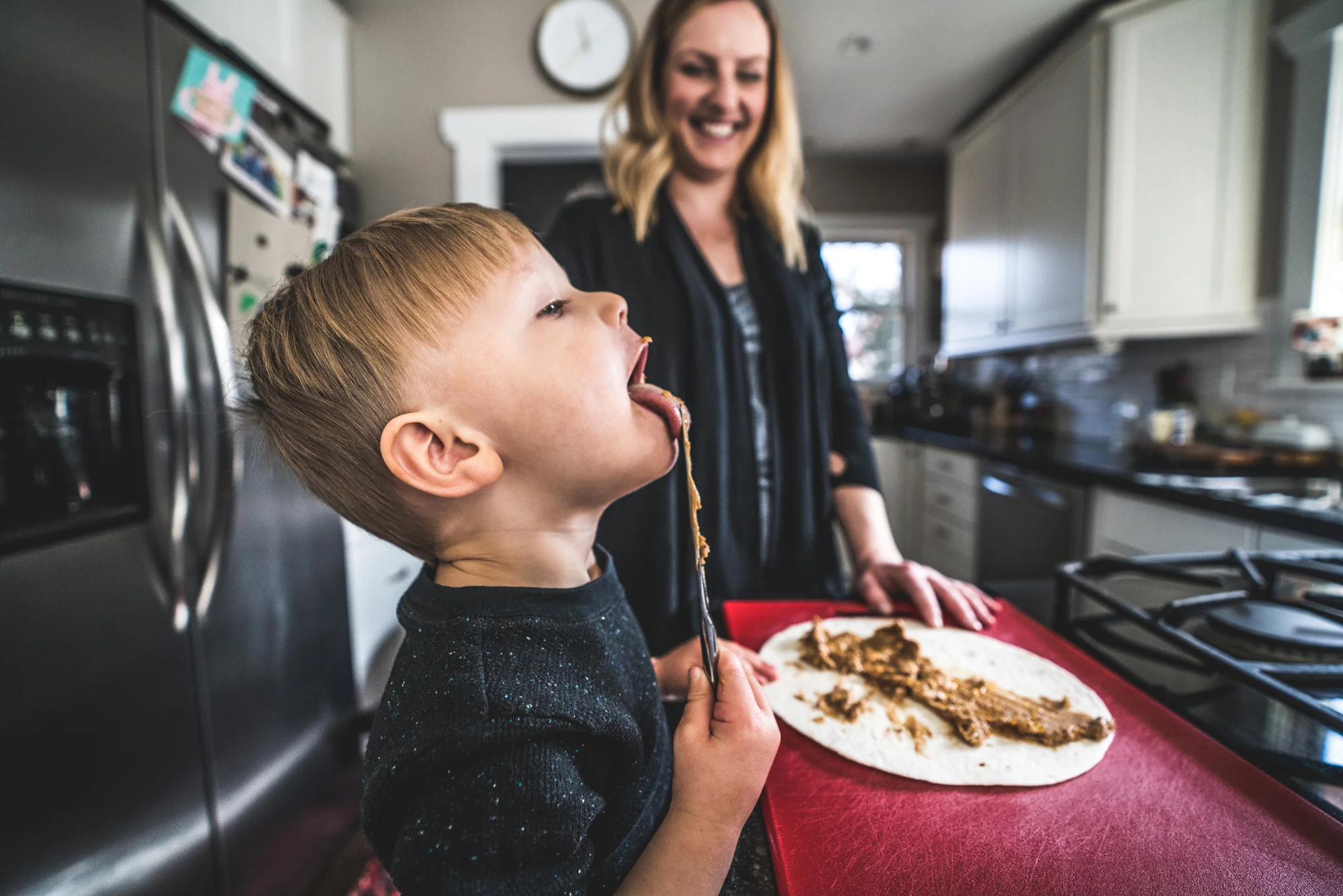 Color close up photo of a little boy licking the peanut butter off of a knife during his family's in-home photography session in Park Hill, Colorado