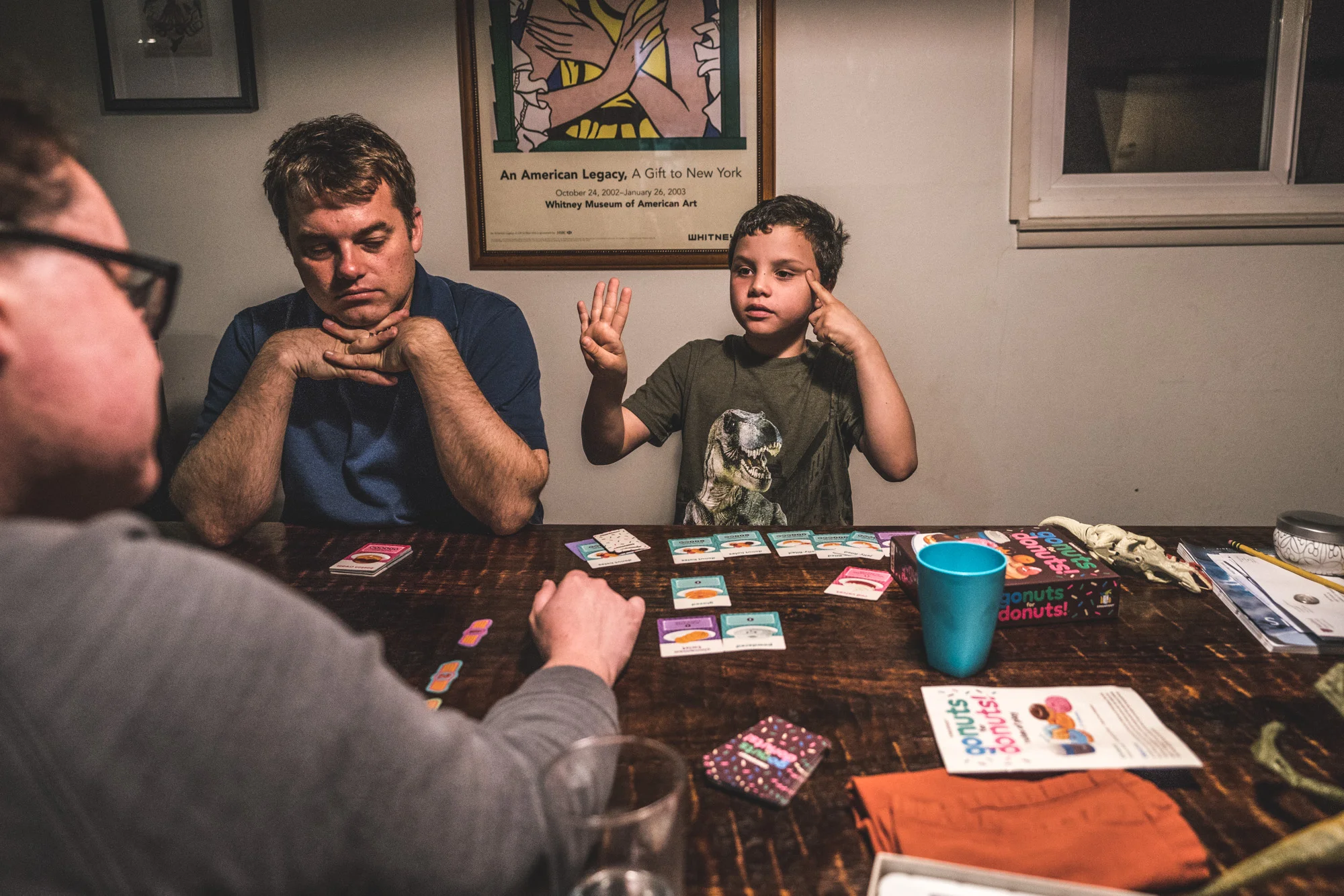 A little boy thinks hard to do the math and add up his points while he plays a card game with his parents at the kitchen table; color photograph taken at the family's home in Oakland, California during their full day in the life documentary photography session.