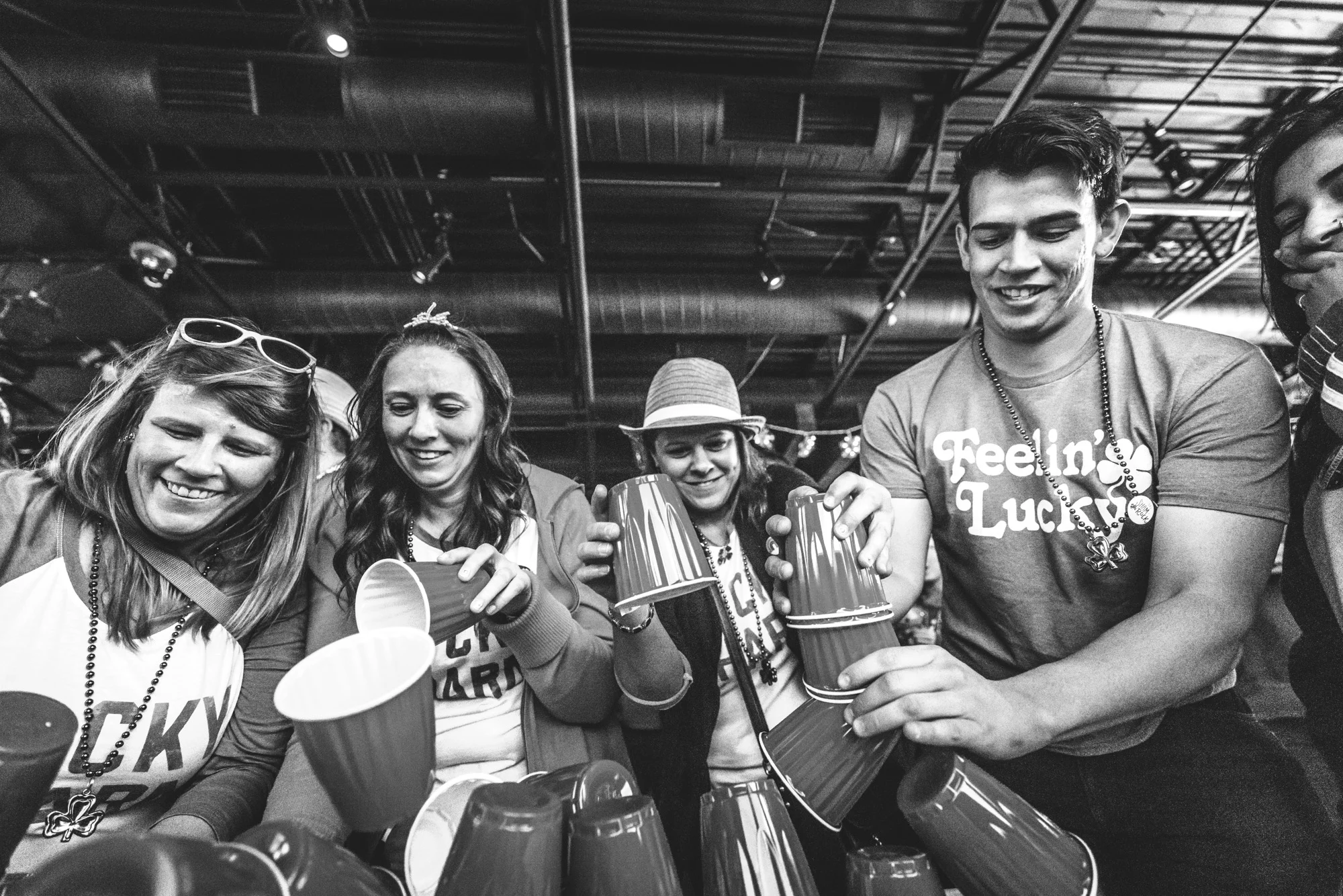 Black and white photo of a group of people wearing St. Patrick's Day attire attempting to stack cups during a pub crawl game at the Autism Society of Colorado's Shamrock Stumble fundraiser in Littleton, CO.