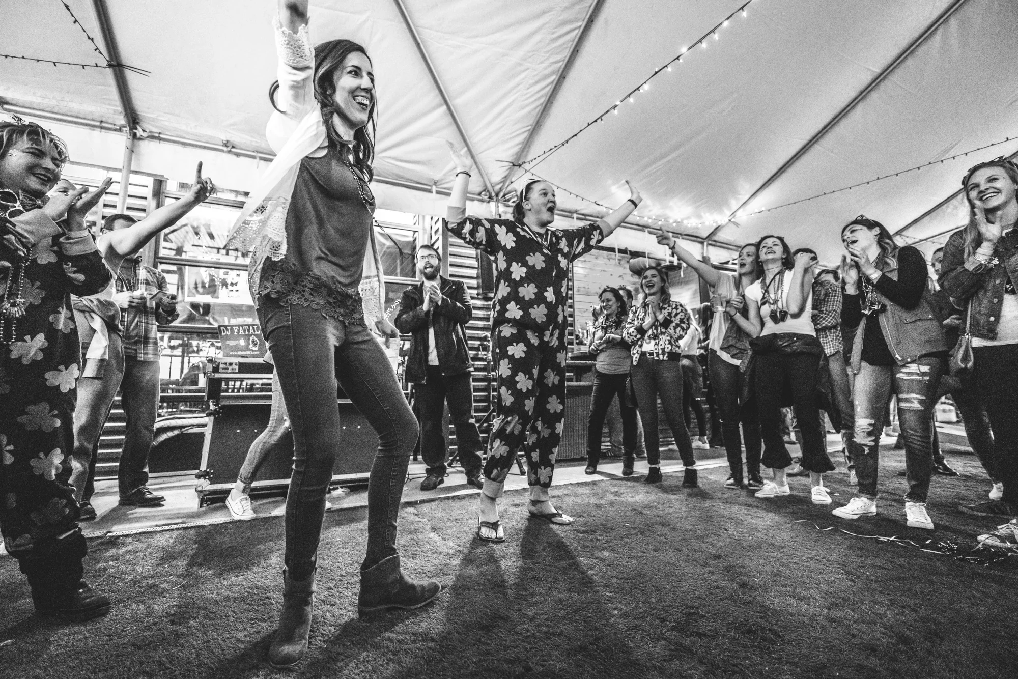 Black and white photo of a group of people in a tent outside of the ViewHouse in Littleton cheering on the woman who helped plan the event. Photograph taken during the ASC Shamrock Stumble pub crawl fundraiser. 
