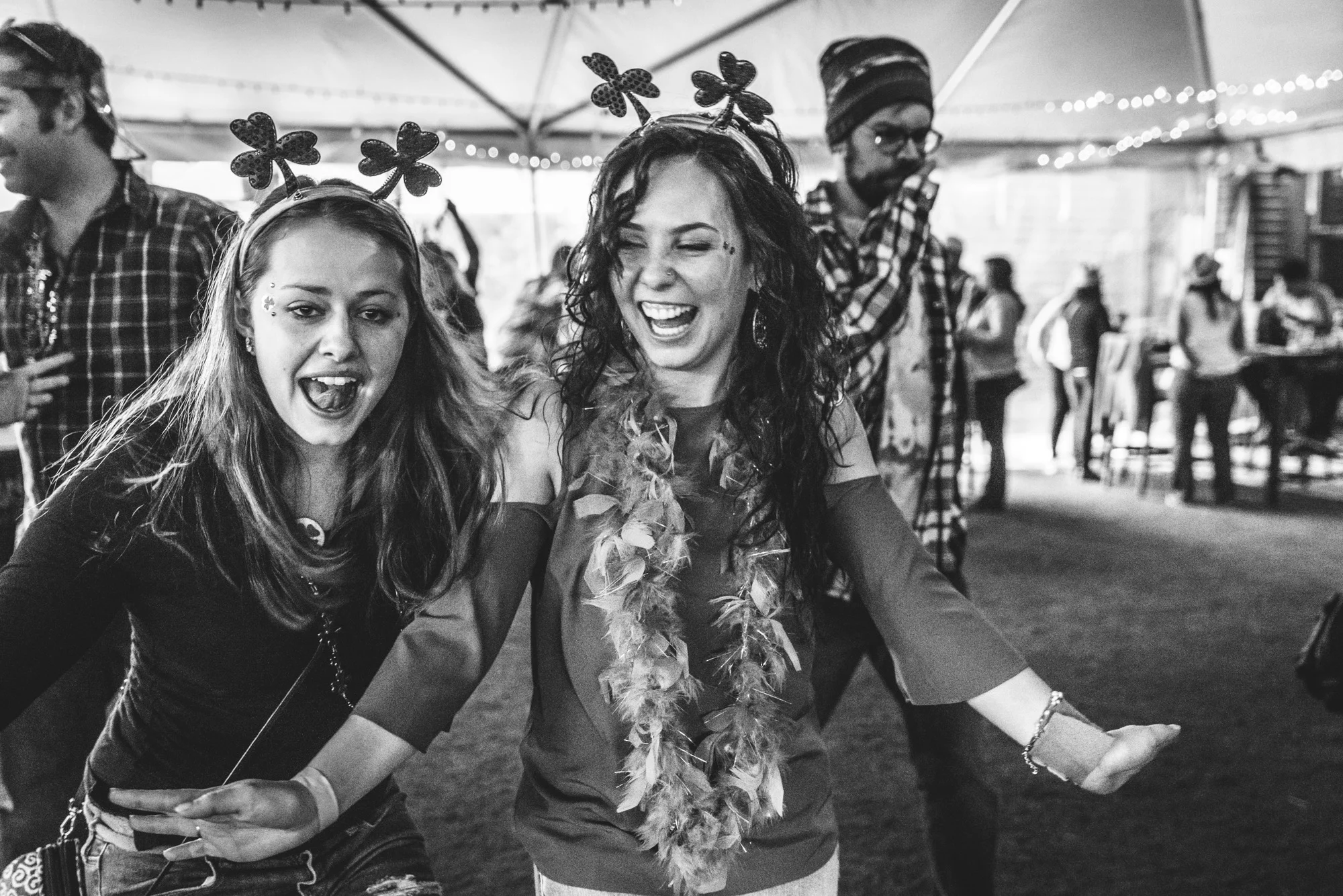 Black and white photo of two women wearing shamrock headbands and laughing and smiling during a charity event for the Autism Society of Colorado in Littleton, Colorado.