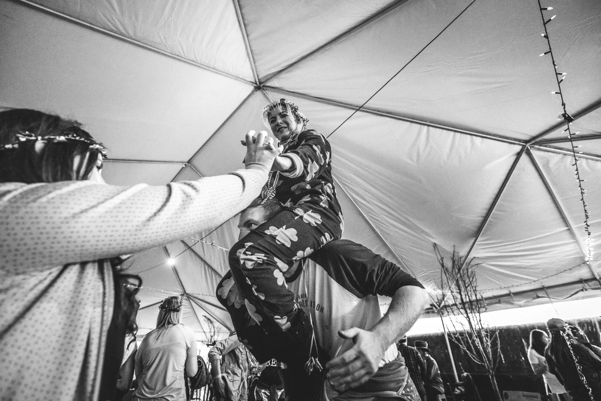 Black and white photo of a woman attempting to climb onto a man's shoulders as they party during the ASC Shamrock Stumble fundraiser event in Littleton, CO.