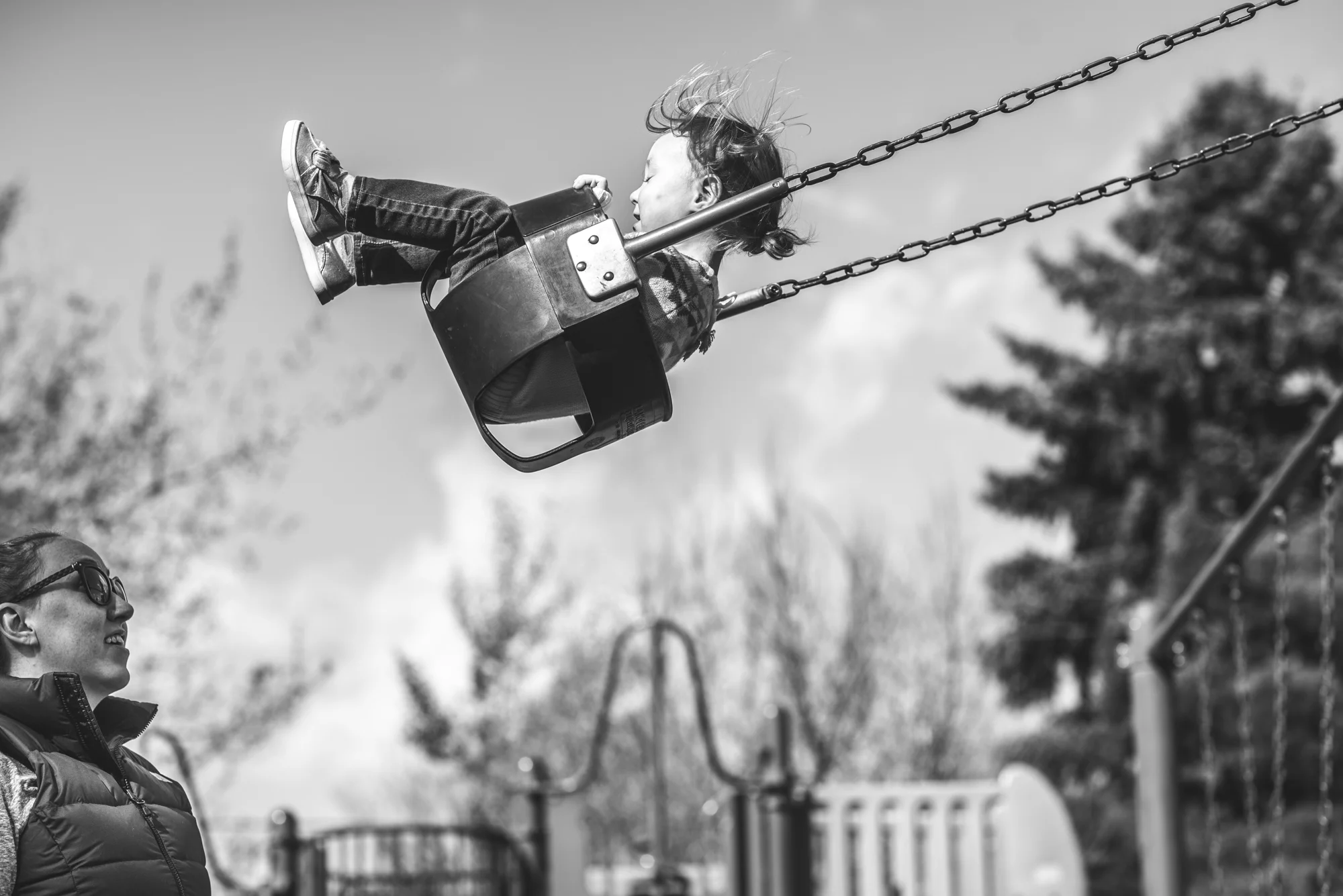 Black and white photo of a little girl swinging high on a swing as her mother watches from below