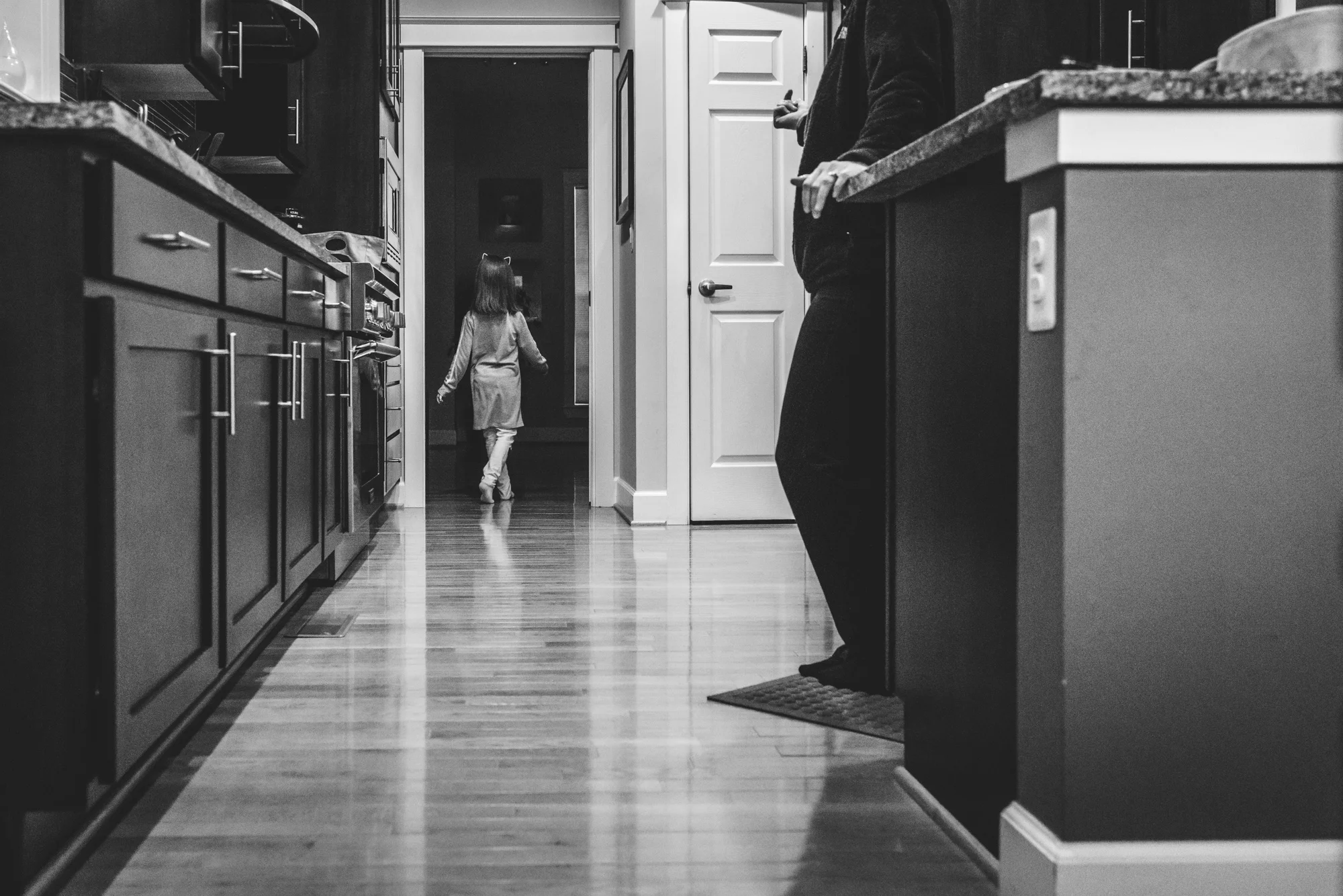 Black and white photo of a little girl sauntering out of her kitchen in Stapleton, Colorado during her in-home documentary photography session