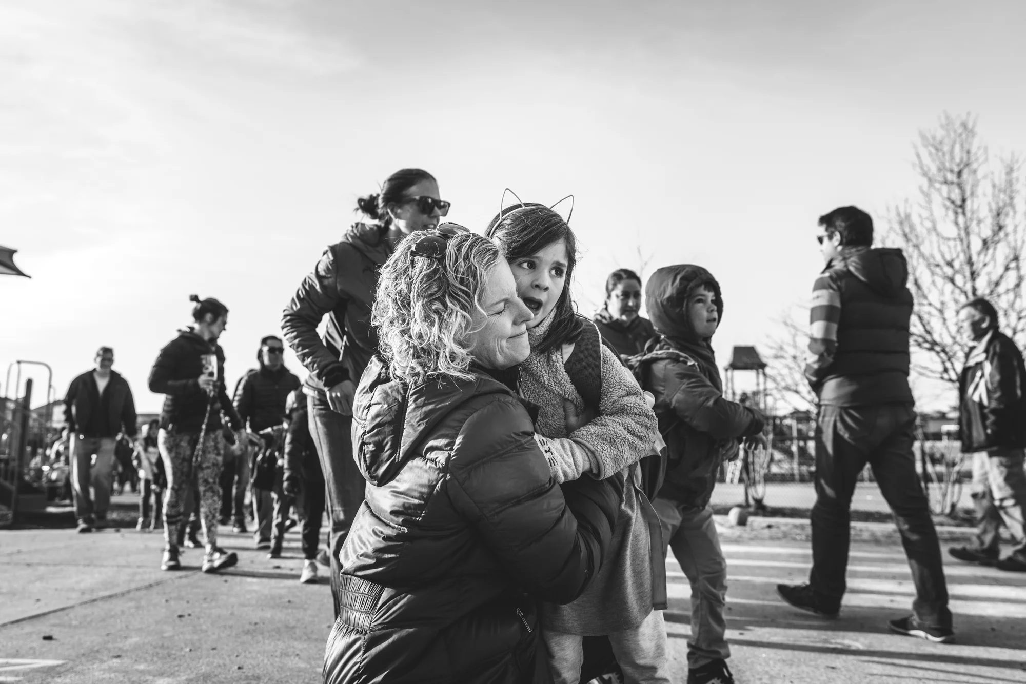 Black and white photograph of a mother and daughter outside of the little girls school in Denver, Colorado, hugging each other goodbye.