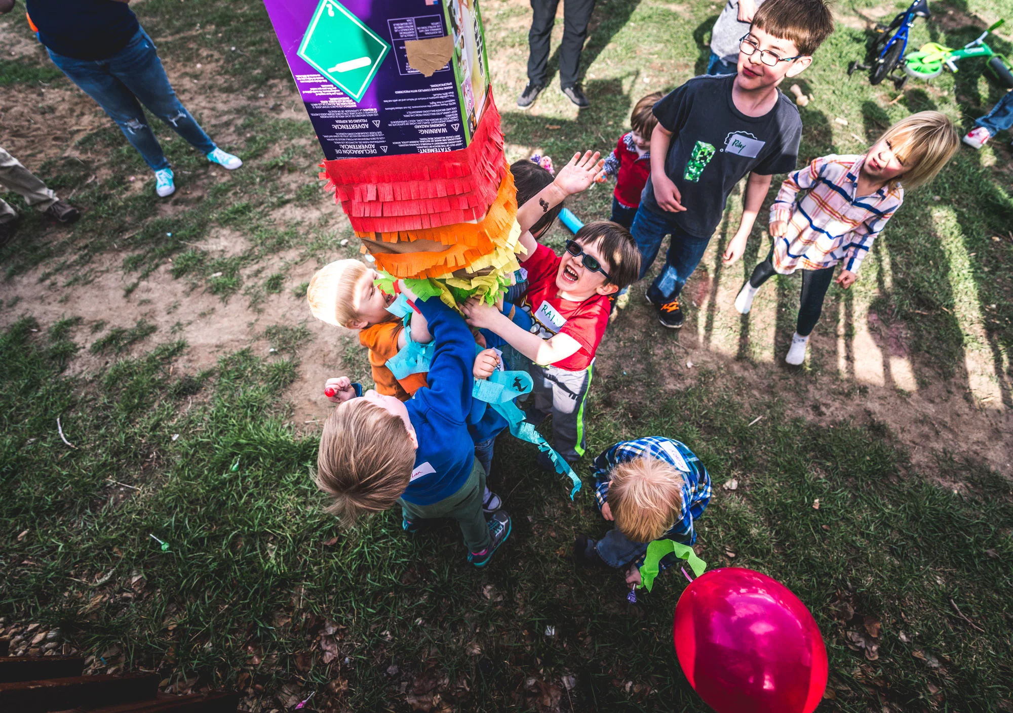 Bright colored overhead photo of a bunch of kids ripping apart a brightly colored piñata in a back yard in Aurora, Colorado