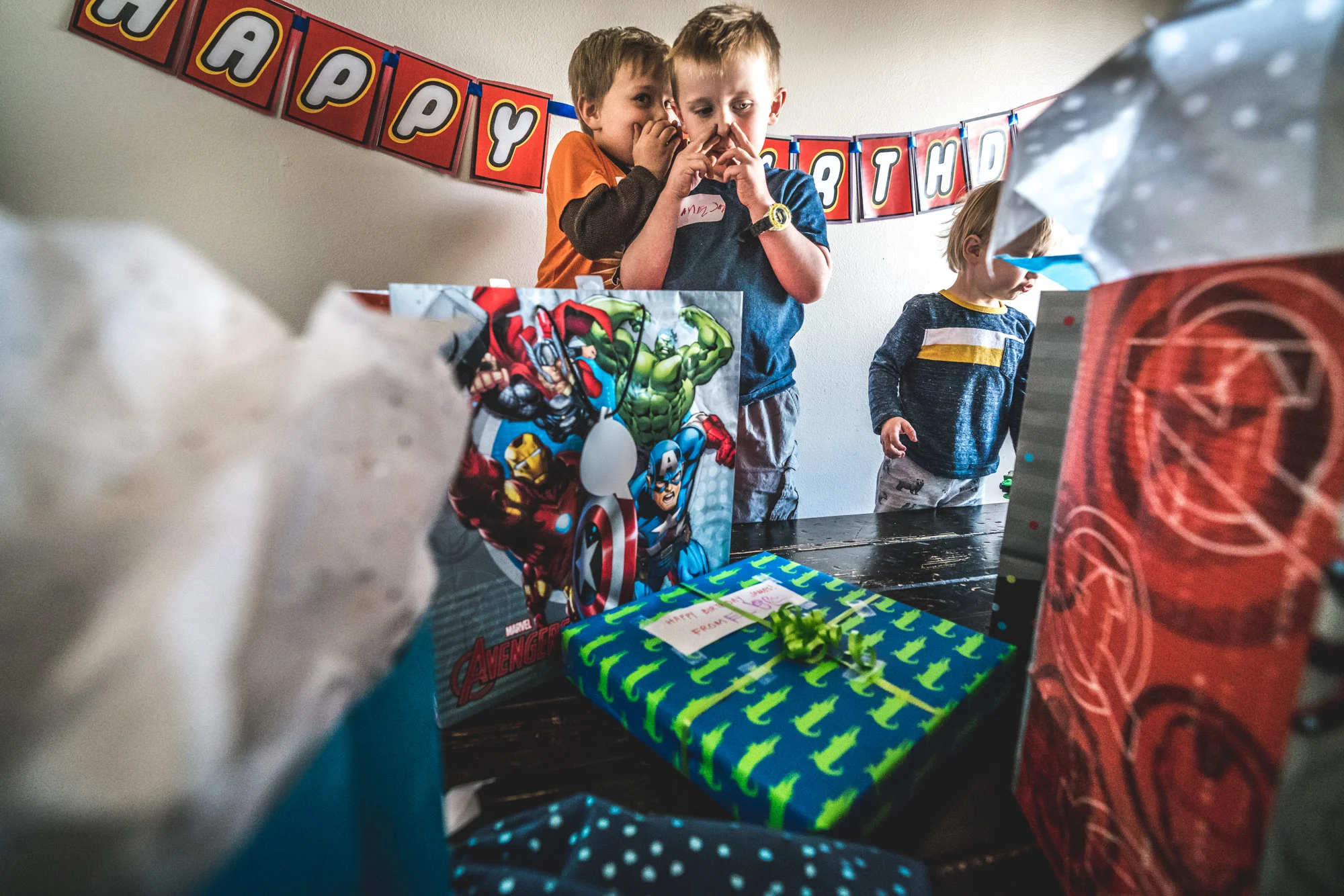 Photo of two little boys surrounded by colorful birthday presents as one little boy whispers to the other