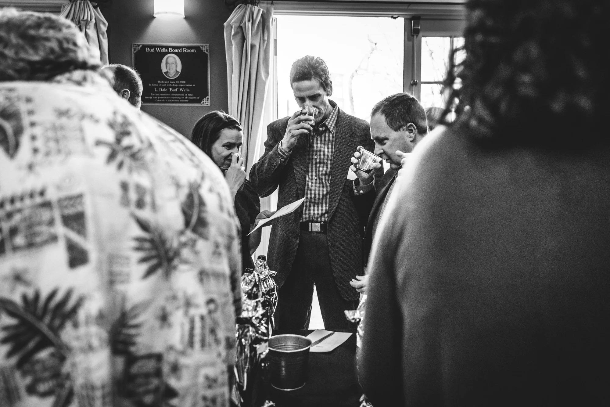 Black and white photo of three people at a competitive wine tasting event for the Wine League, smelling their wine. Photo taken at the Colorado Automobile Dealer's Association in Denver, Colorado.