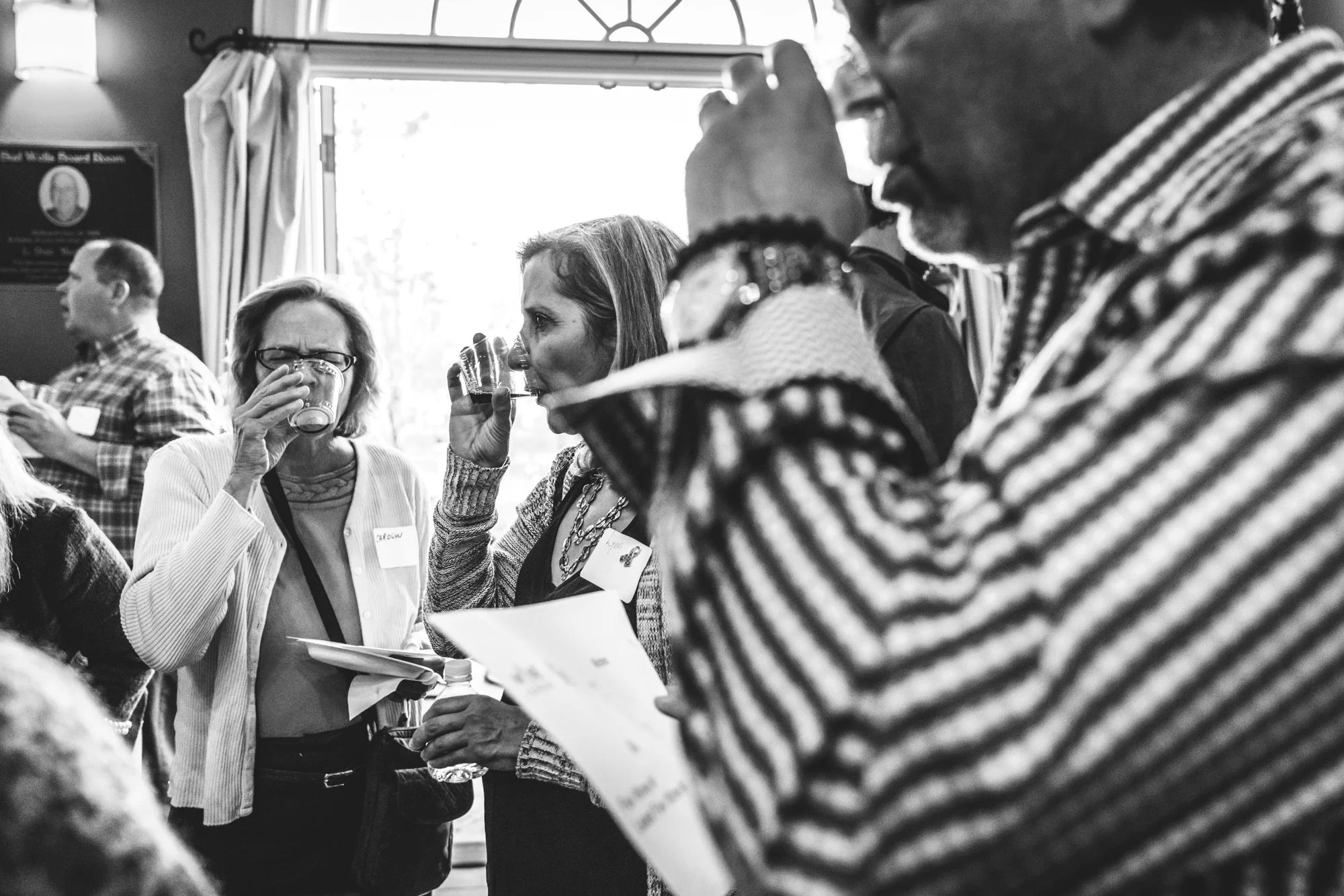 Black and white photo of three individuals taking a drink of wine during the WineLeague wine tasting fundraiser for the Autism Society of Colorado.
