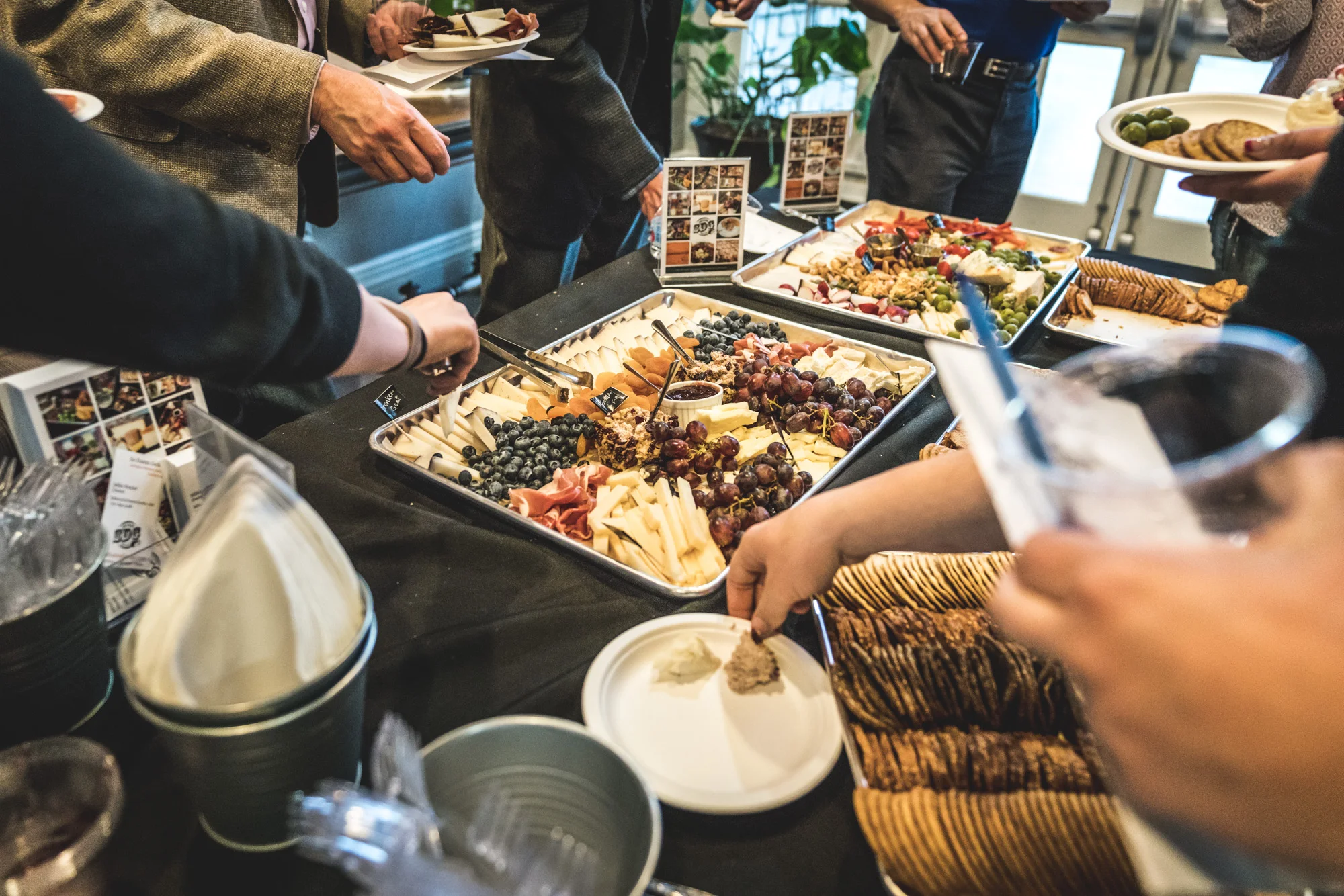 Color photo of beautiful meet and cheese trays on a table as people reach in to grab food. Taken during the Autism Society of Colorado's Wine Competition event in Denver, Colorado