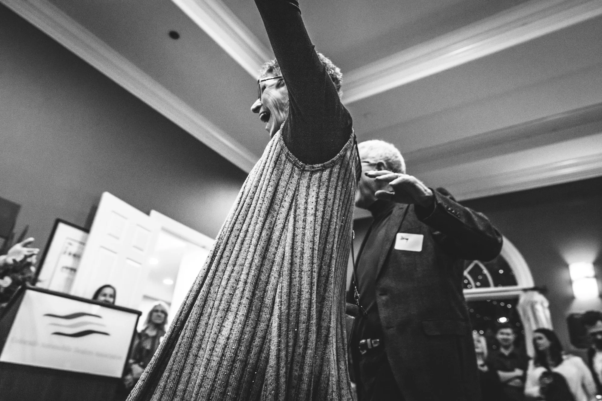Black and white photo looking up at a woman as she raises her arms with joy and smiles wide. Taken at a non-profit wine event in Denver, Colorado.