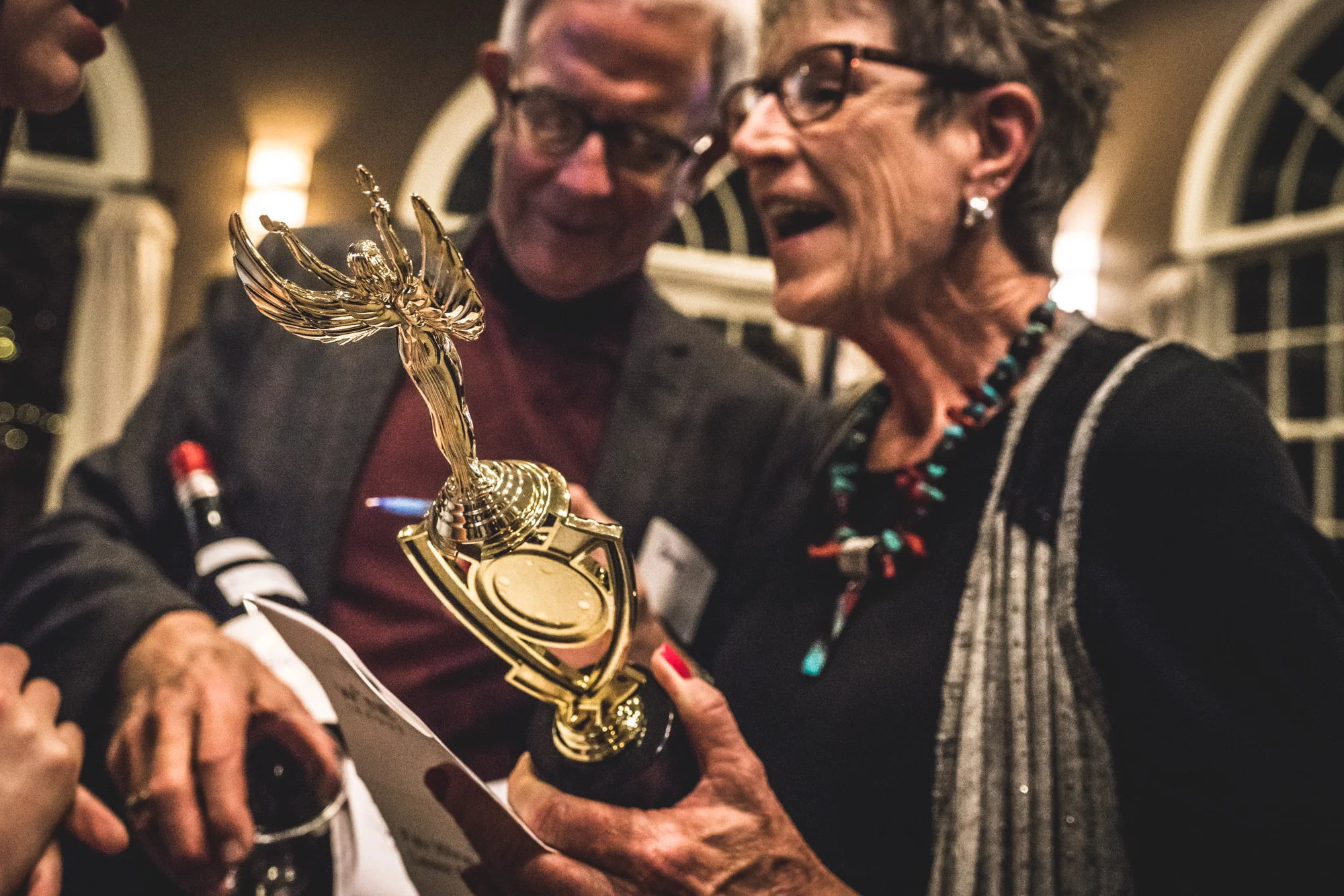 Color photo of a woman and man holding the trophy they won at a competitive wine drinking competition in Denver, CO.